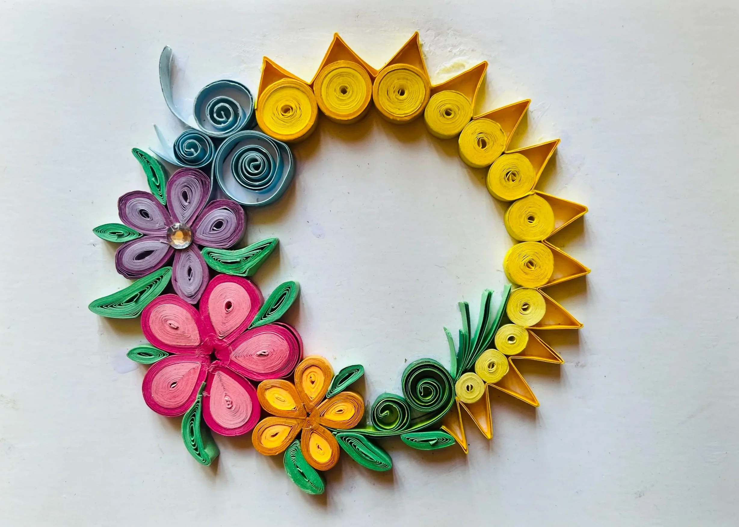 a partial wreath of flowers and sun rays with tightly wound paper in the style of paper quilling