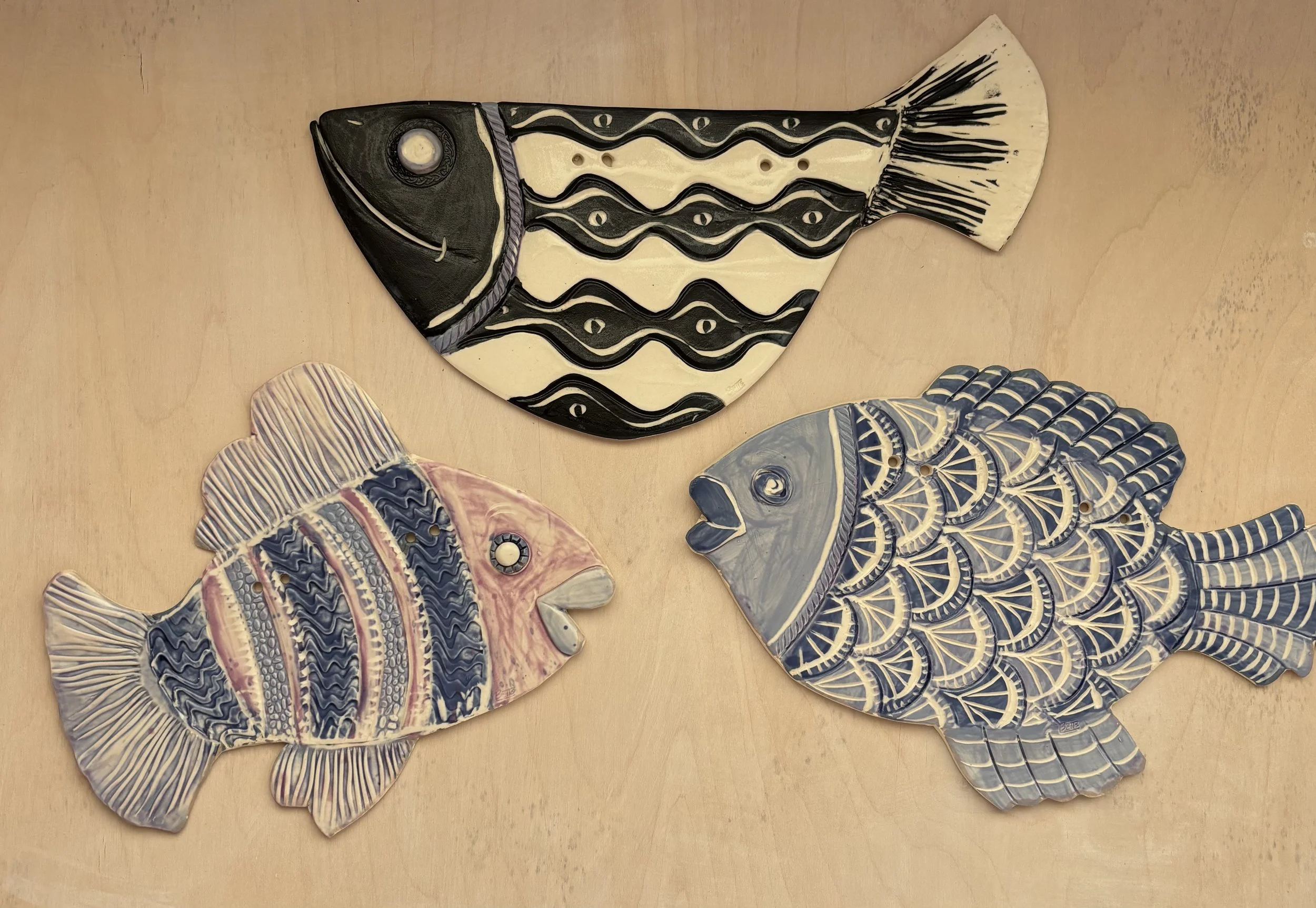 a photo of three clay fish with varying colors, shapes, and patterns