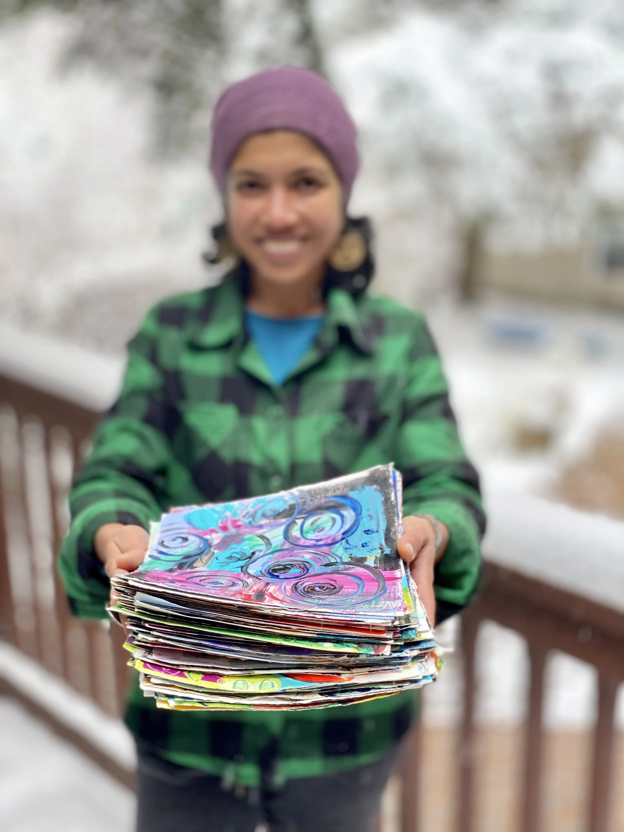 Artist Surabhi Pandey holding a pile of abstract paintings on paper