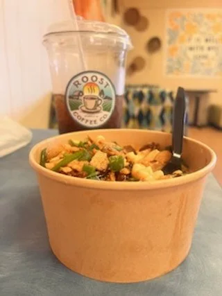 A bowl of macaroni and cheese with broccoli, and a plastic cup of iced coffee with a straw and a Roost Coffee logo.