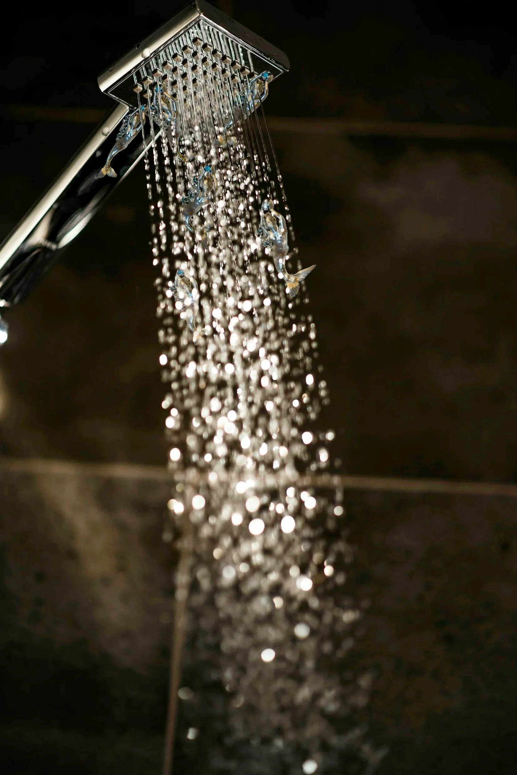 Close-up of a shower head with water streaming down, reflecting light and creating a sparkling effect.