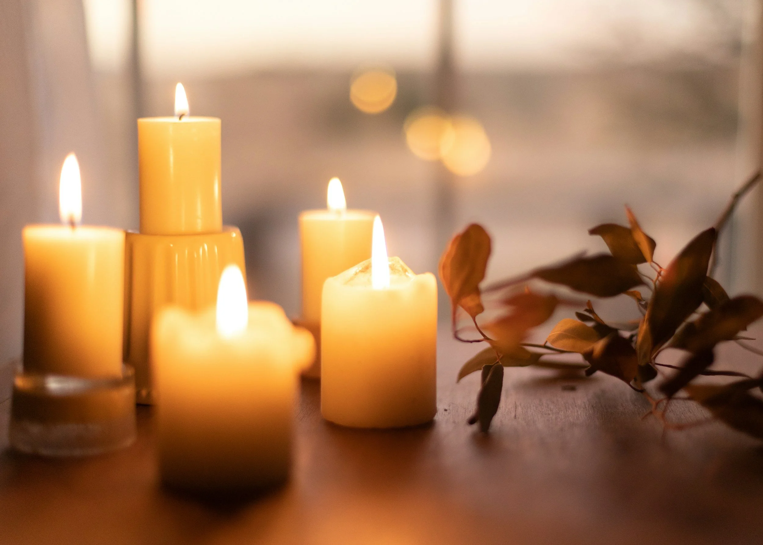 Lit candles on a table with decorative leaves in the background.