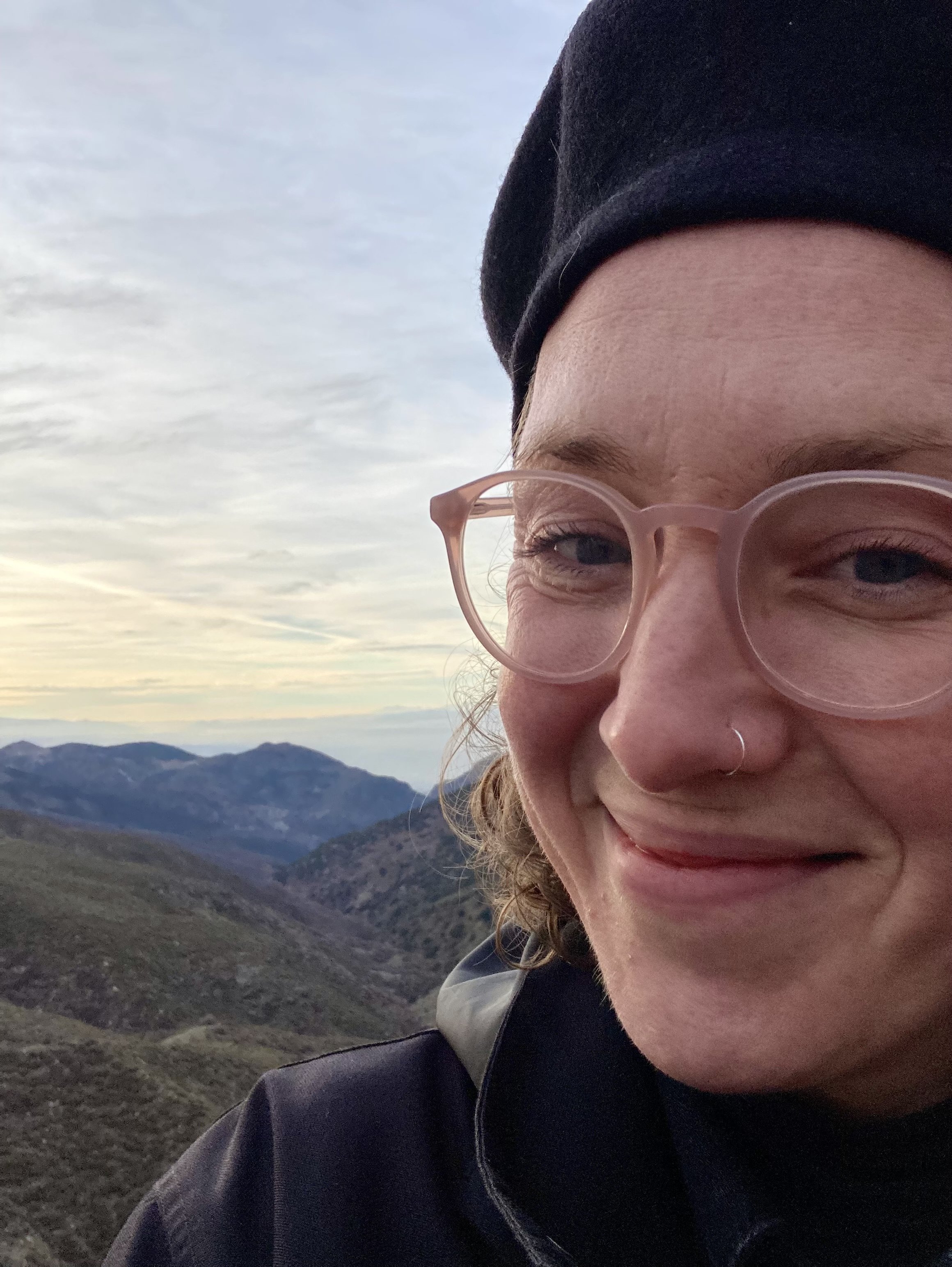 A photo of me (Adelle) wearing glasses and a hat with a mountain view behind me