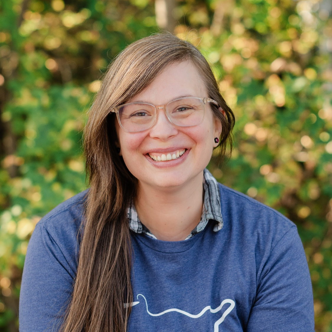 A woman with long brown hair and glasses smiling at the camera.