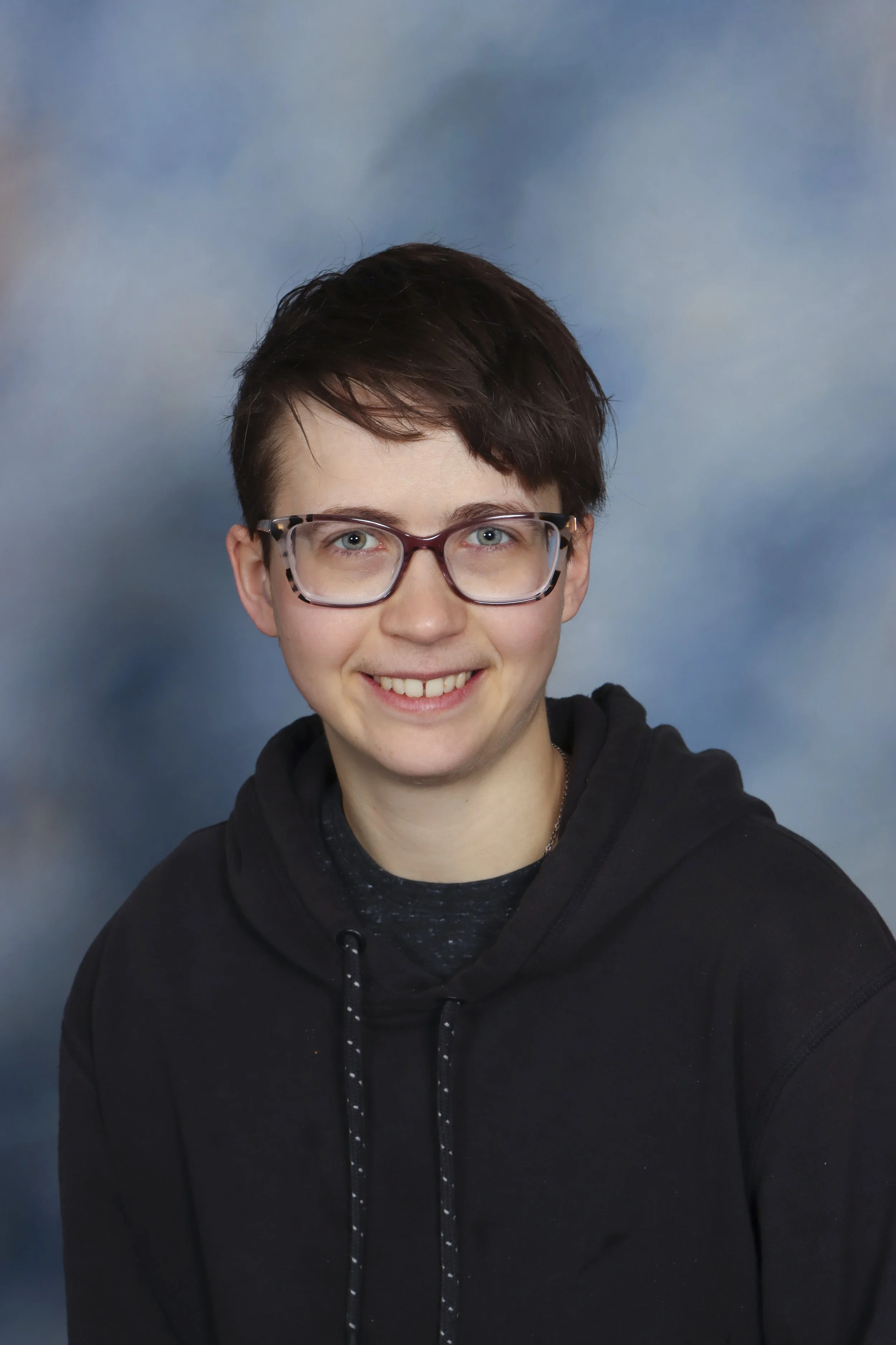 A young person with curly hair and glasses holding a violin while sitting at a piano.