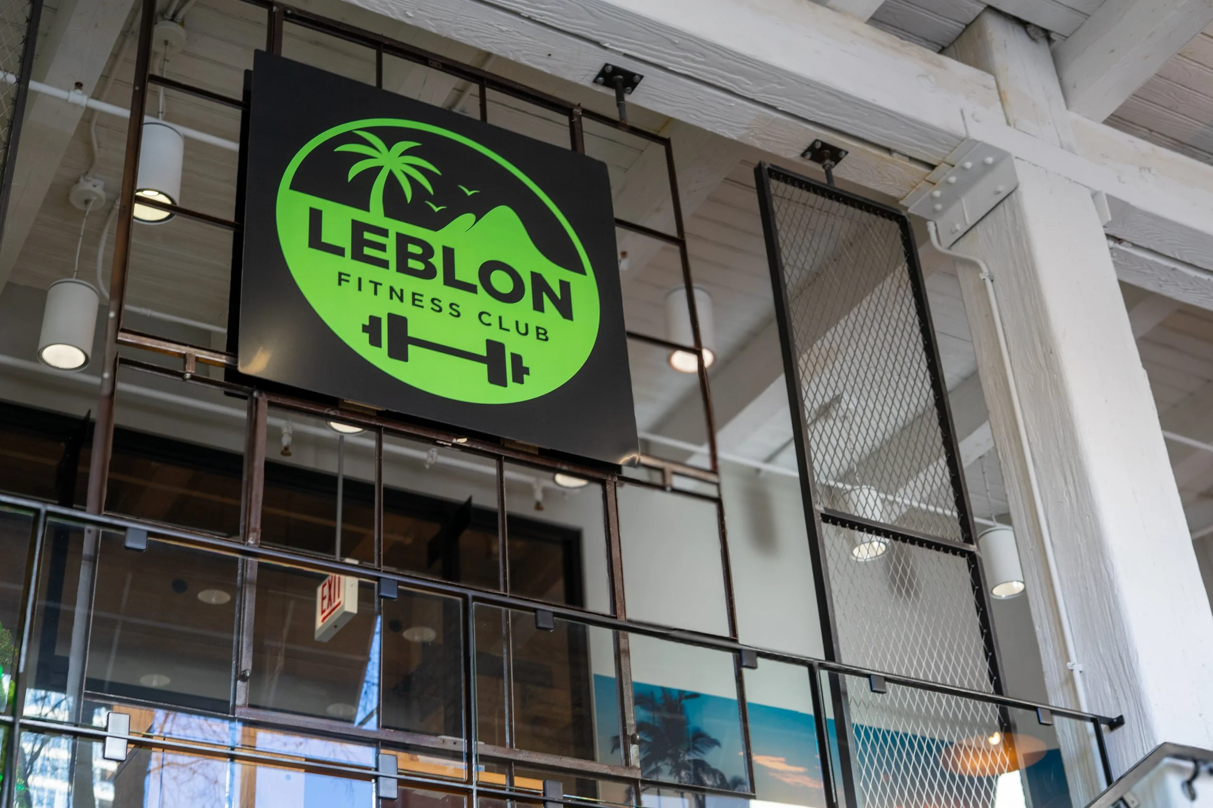 Sign for Leblon Fitness Club with a palm tree, mountain, and barbell logo.
