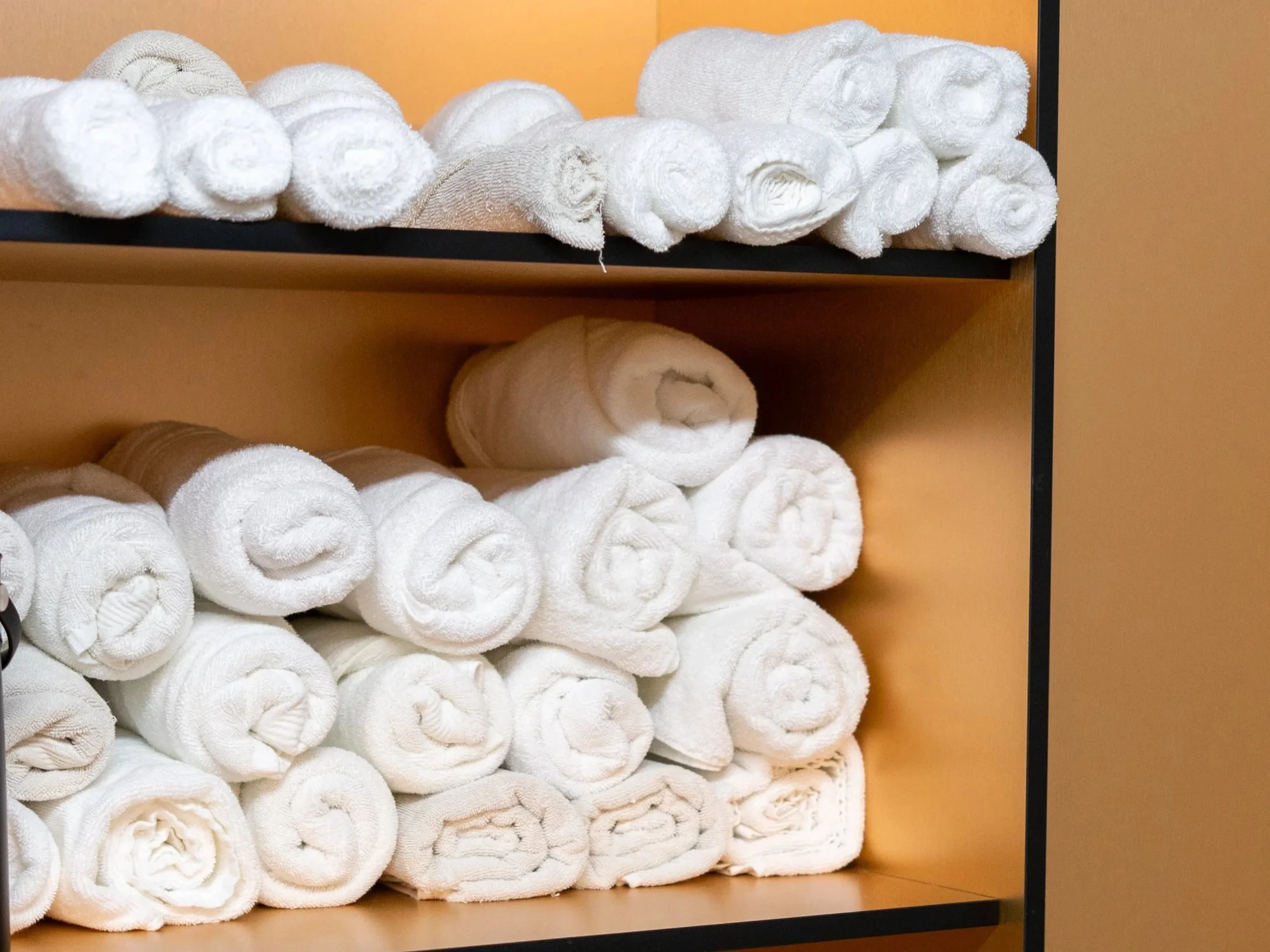 Shelves filled with neatly rolled white towels in a spa or hotel setting.