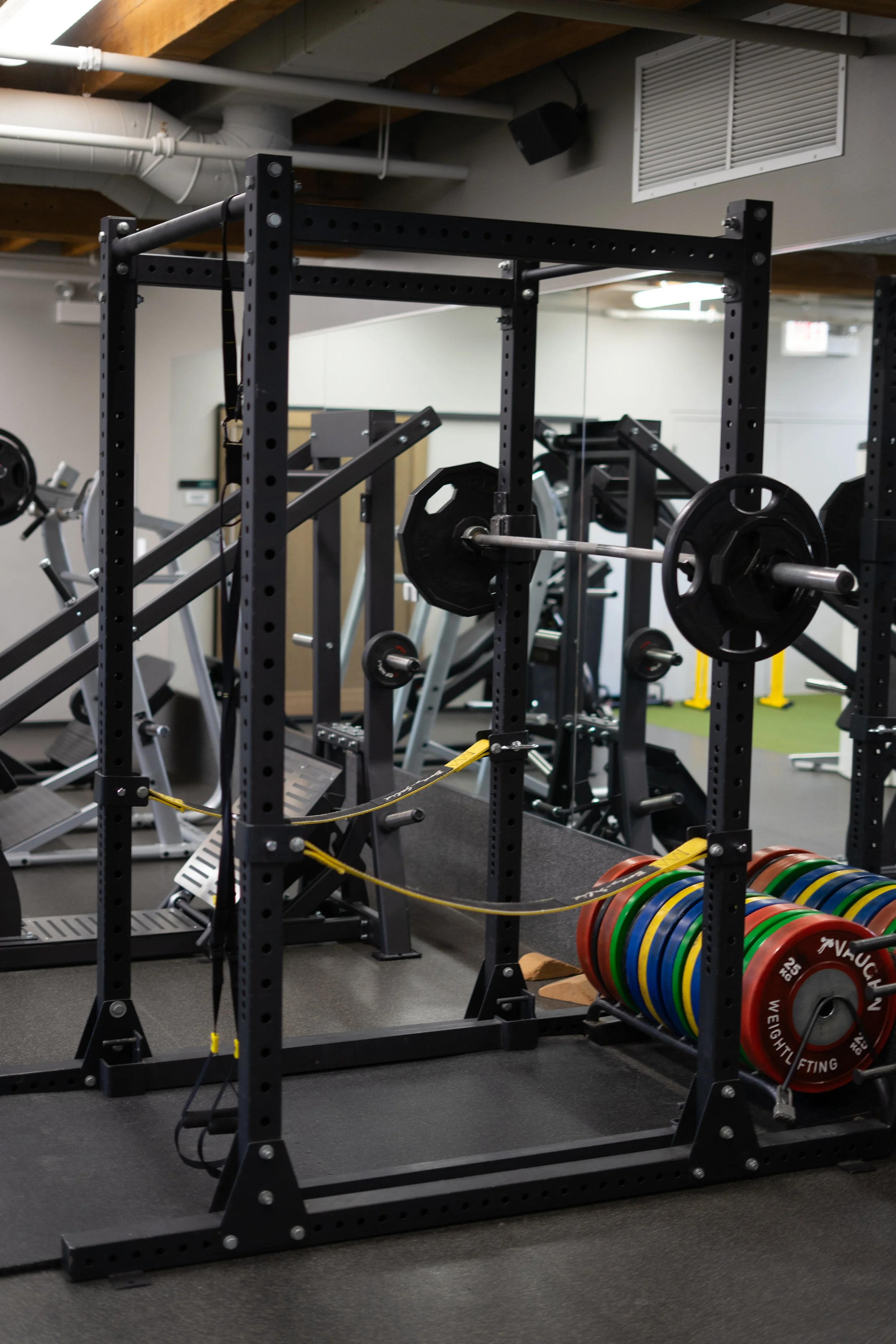 Empty gym with weightlifting equipment, including a squat rack, weight plates, and barbells.