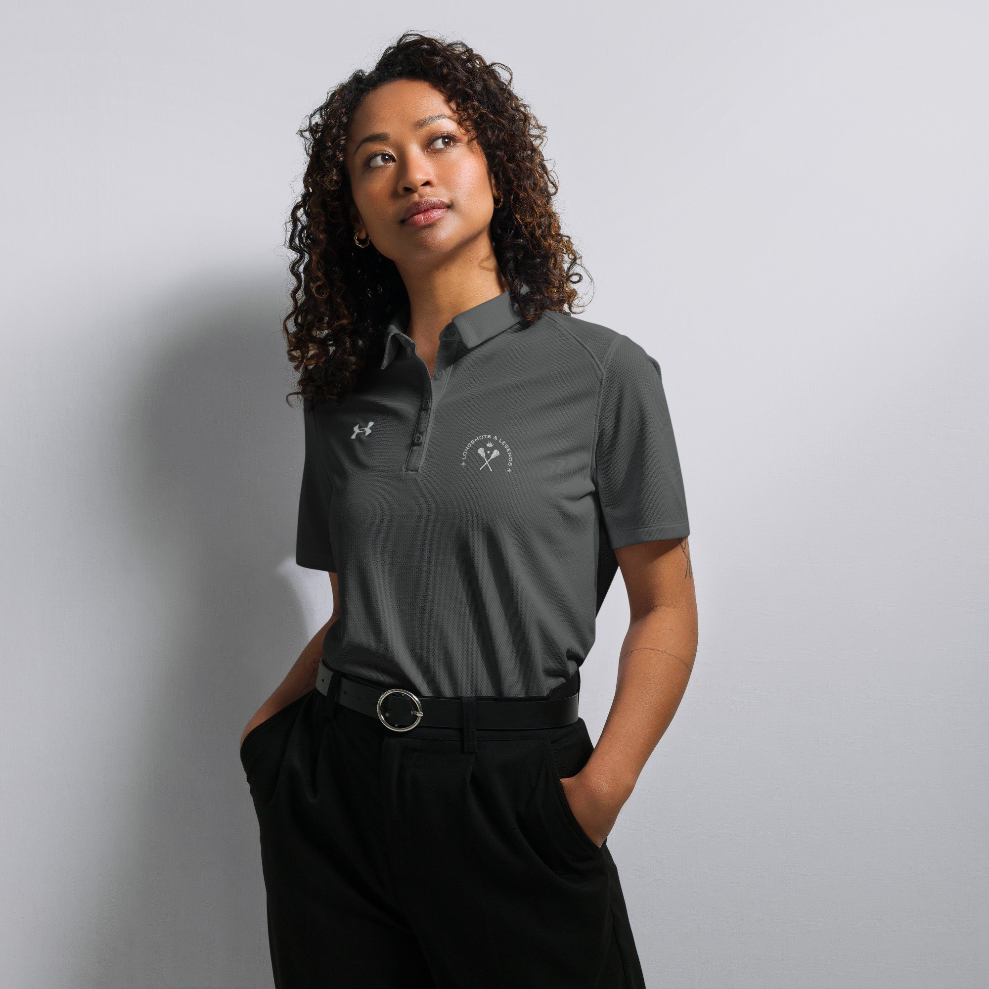 Custom embroidered women’s Under Armour® collared polo shirt with lacrosse logo in dark gray. Celebrate with the Longshots and Legends collection of athletic wear.