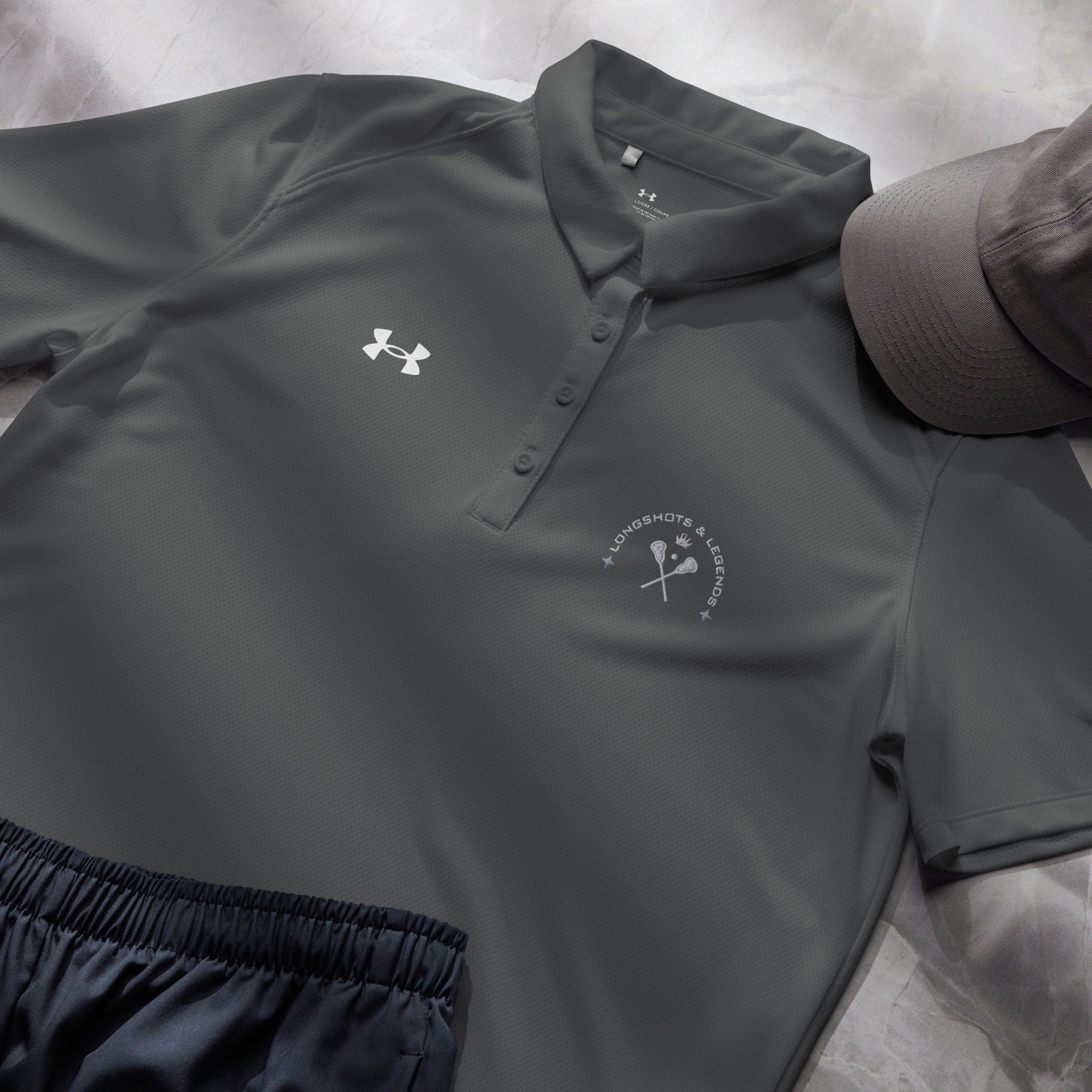 Custom embroidered women’s Under Armour® collared polo shirt with lacrosse logo in dark gray. Celebrate with the Longshots and Legends collection of athletic wear.