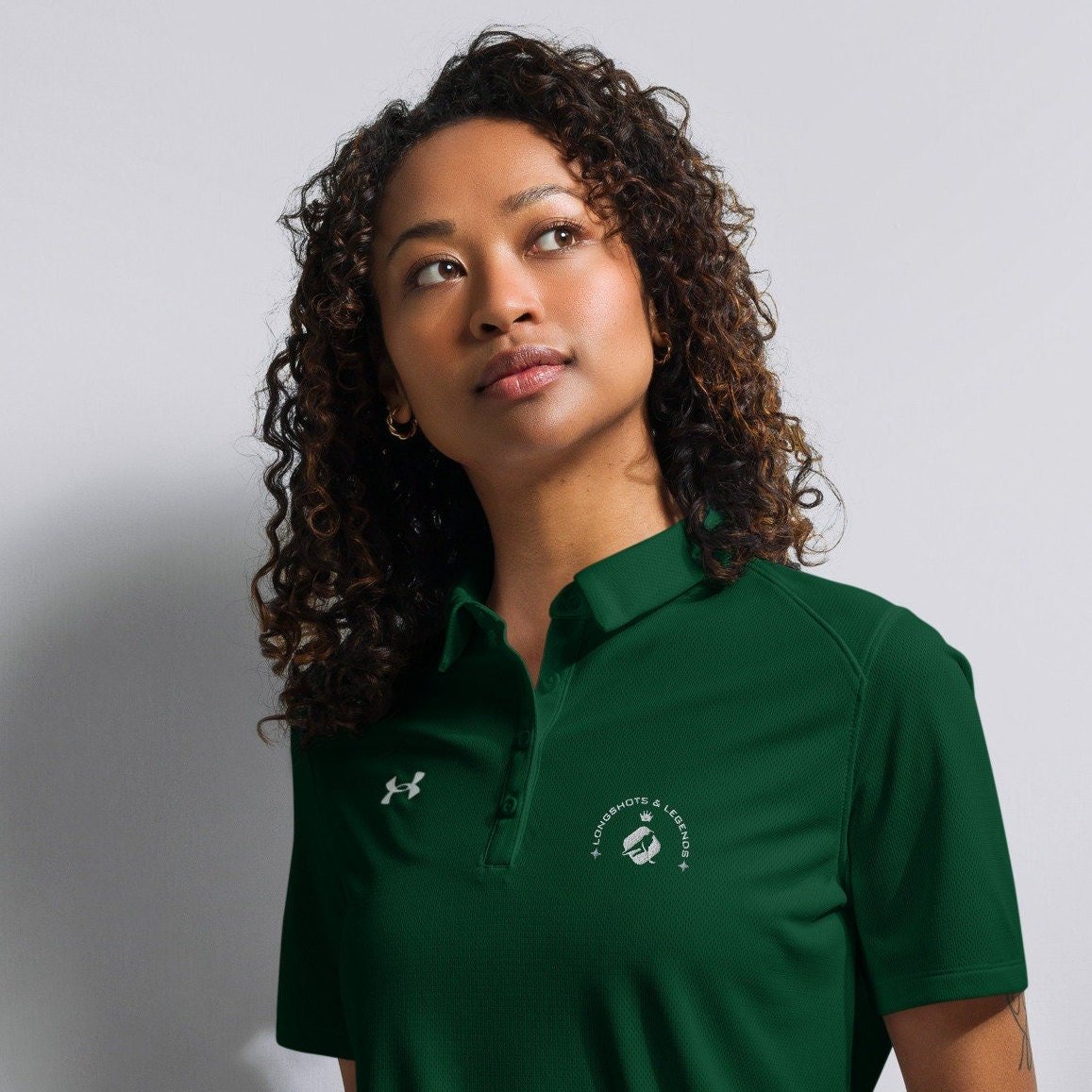 Custom embroidered women’s Under Armour® collared polo shirt with hockey logo in spruce green. Celebrate with the Longshots and Legends collection of athletic wear.
