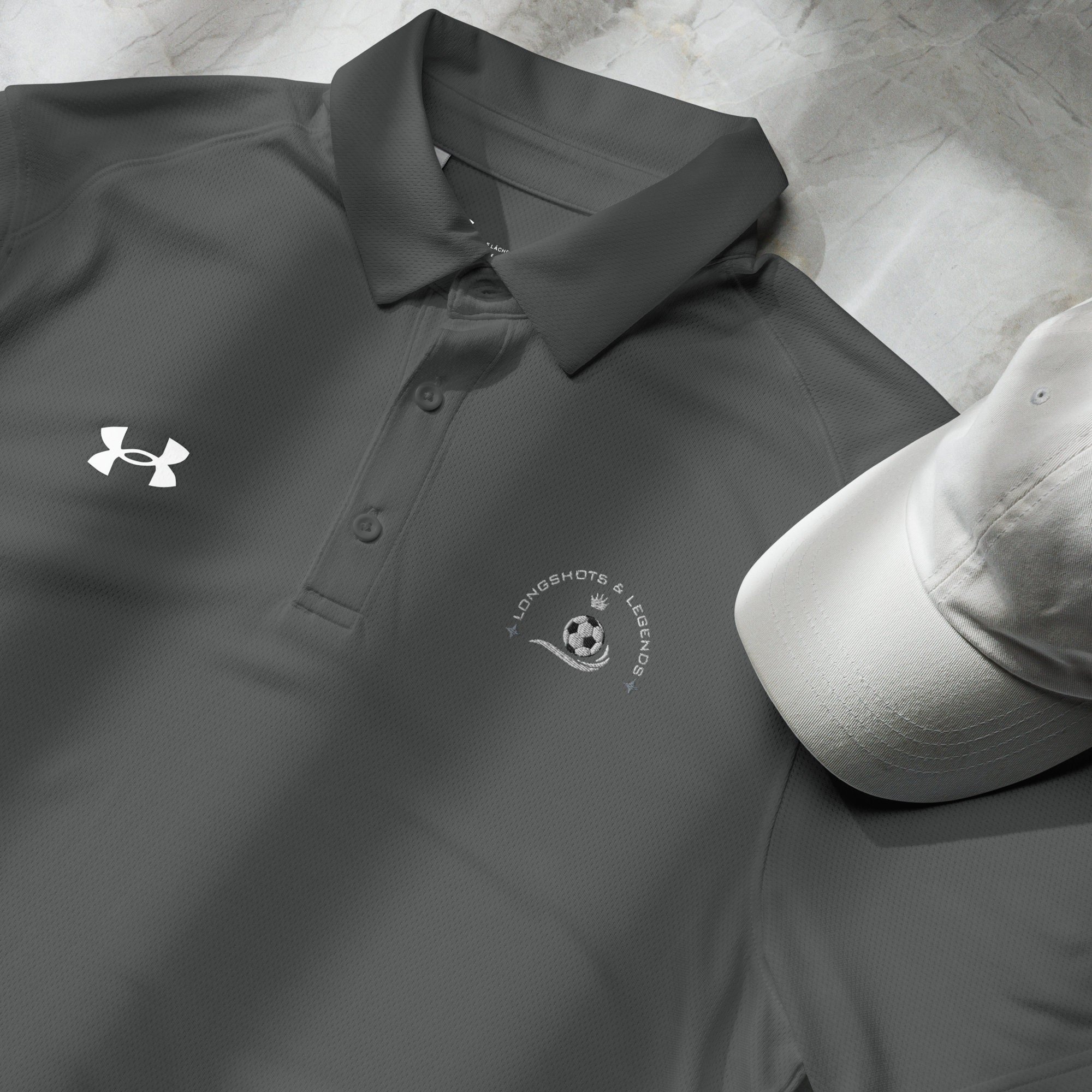 Custom embroidered men’s Under Armour® collared polo shirt with soccer logo in dark gray. Celebrate with the Longshots and Legends collection of athletic wear.