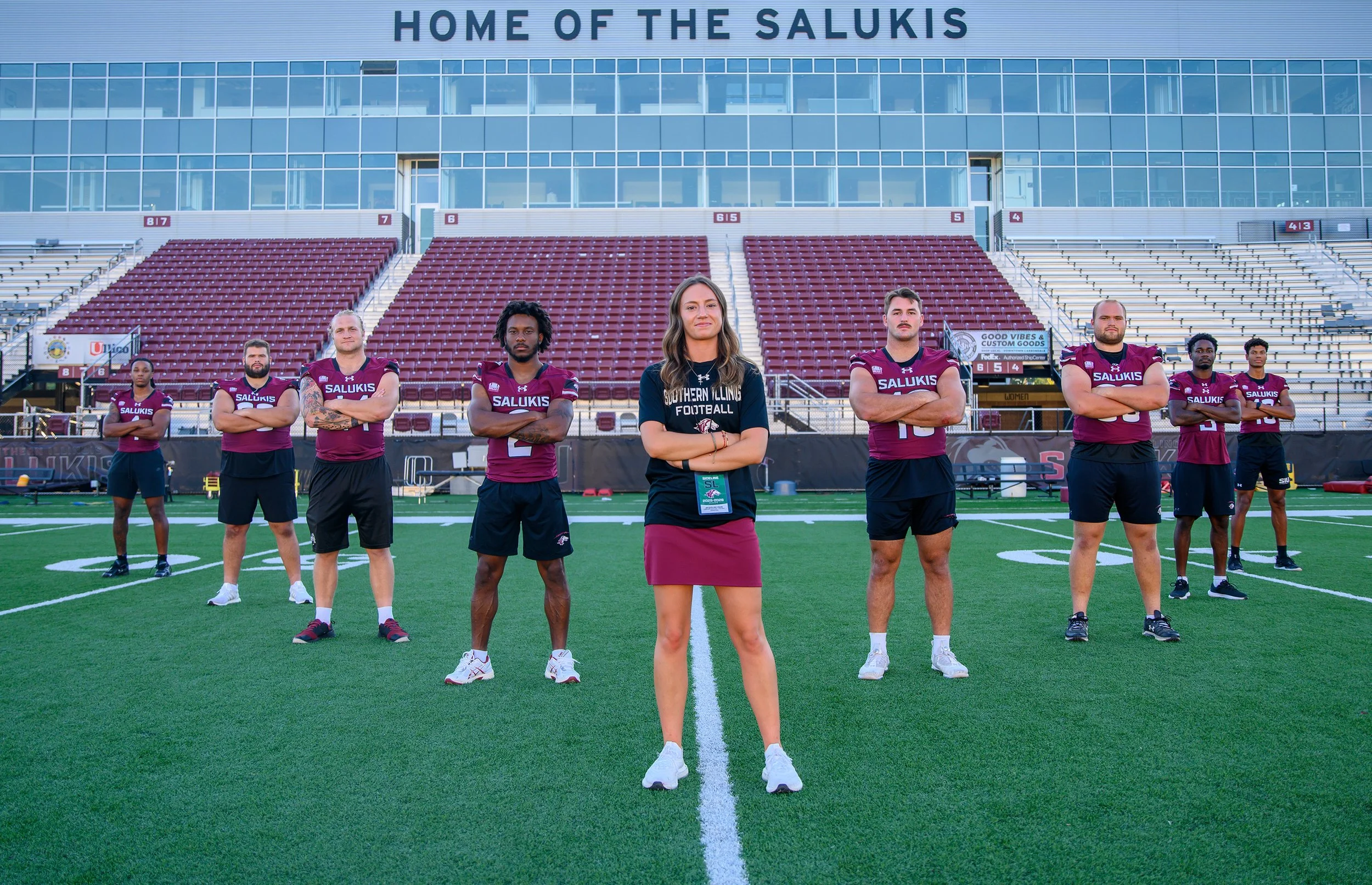 Jacqueline Crain, assistant director of football operations, 22, poses for a portrait with senior SIU football players Wednesday Sep 17, 2025 at Saluki Stadium in Carbondale, Ill. “Coach Hill asked me one day before a team meeting when I graduated. H