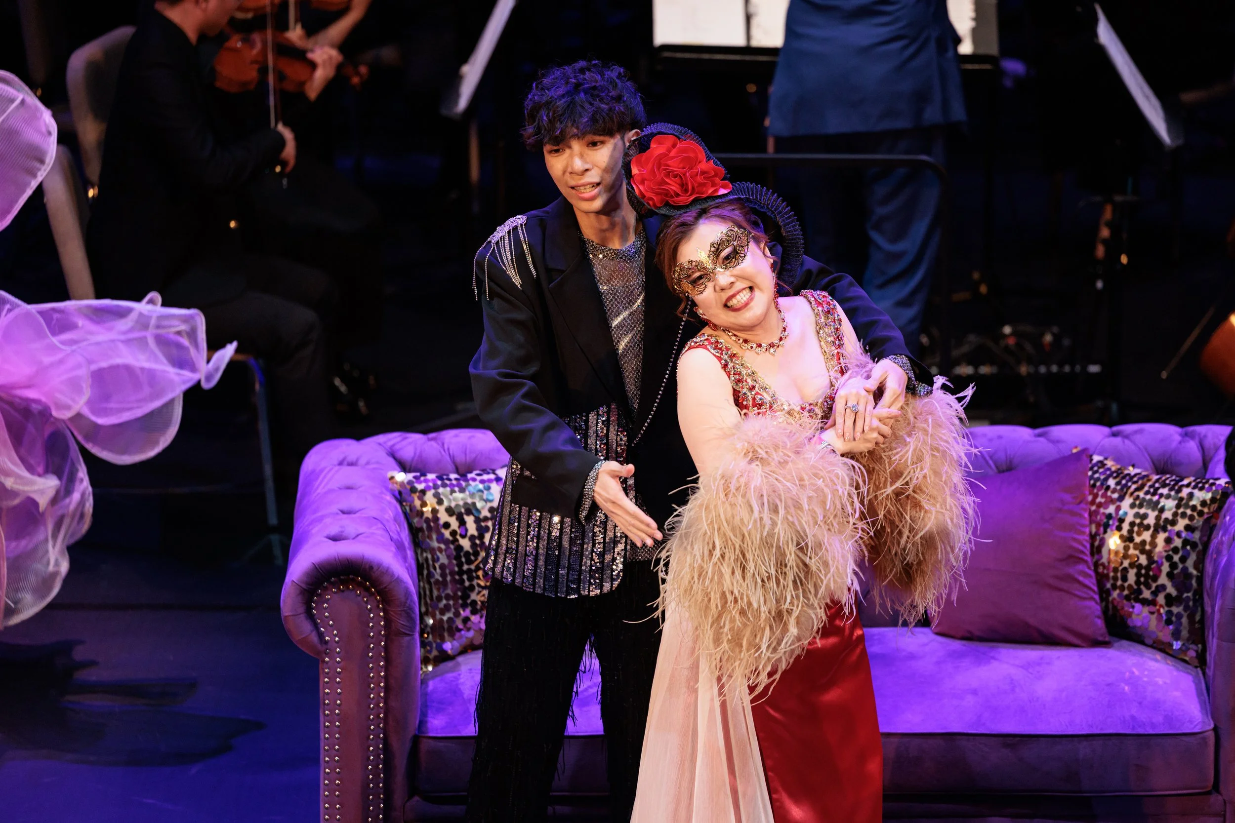 A young man and an older woman dressed in theatrical costumes are on stage.