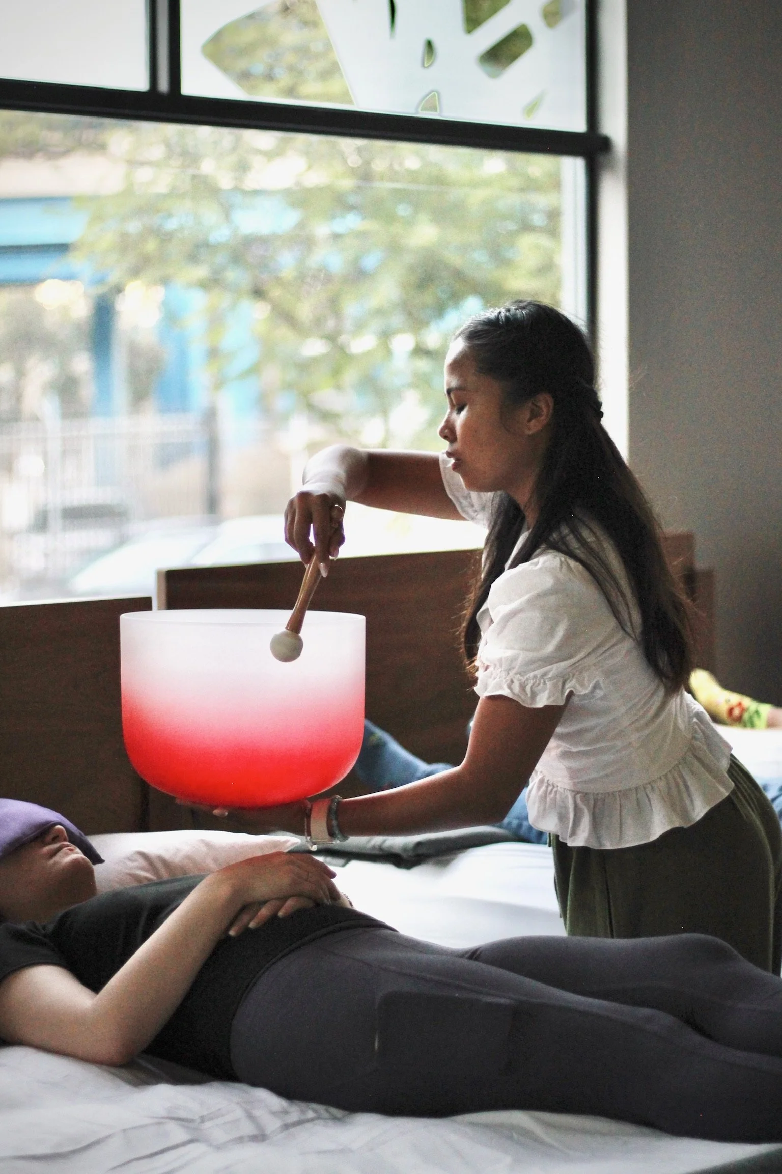 Avril of Well With Avril playing a crystal singing bowl close to a female guest for targeted vibrational sound therapy in McRoskey Mattress Co. San Francisco.