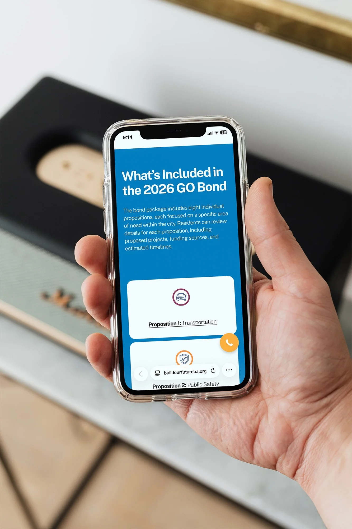 A person holding a smartphone displaying a webpage about the 2026 GO Bond proposals, with icons and navigation buttons.