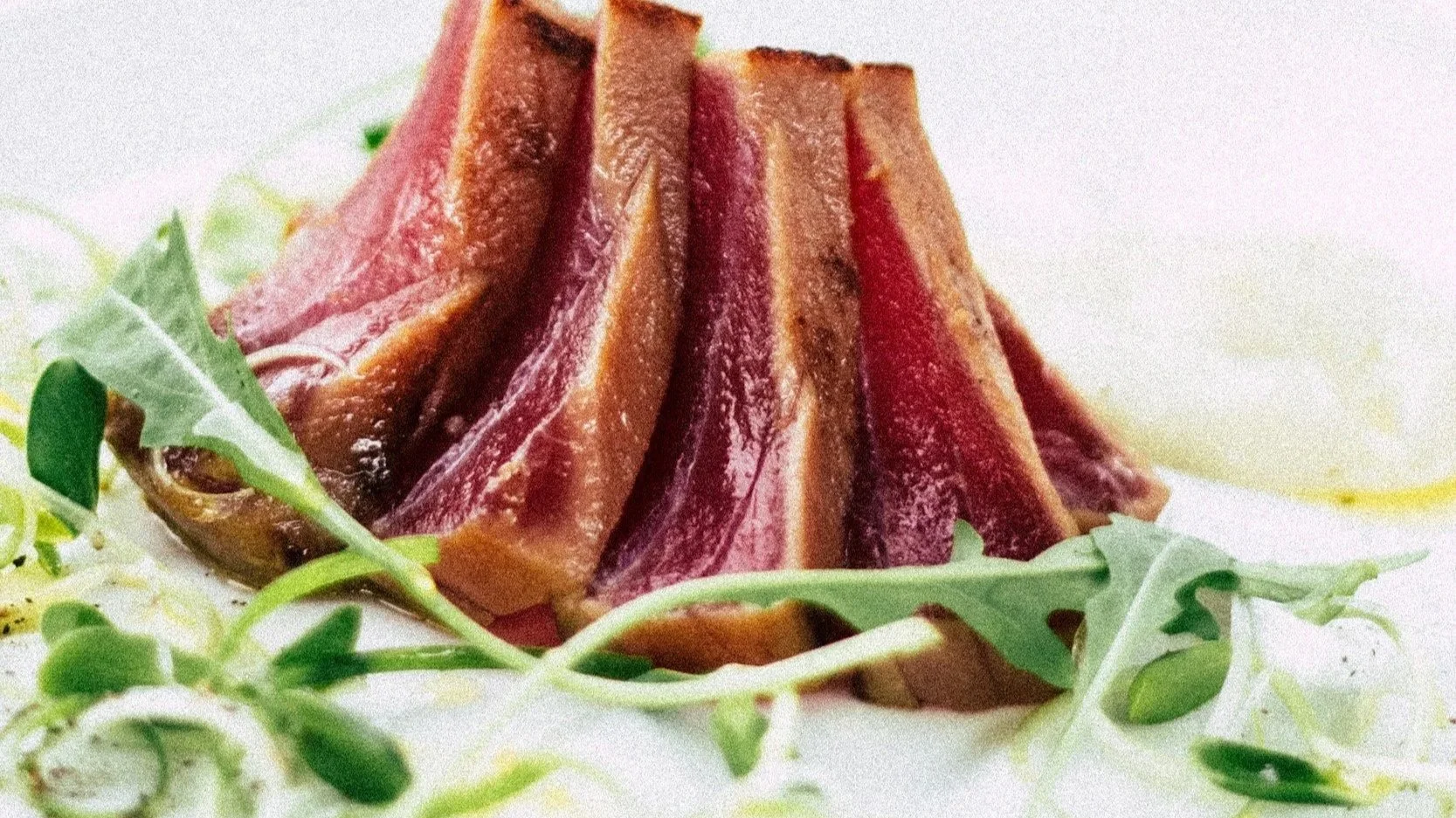 Slices of raw tuna arranged in a pyramid shape on a white plate, garnished with fresh green arugula leaves.