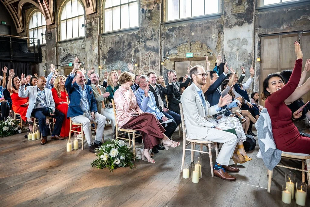 Multiple rows of guests, some with their hands raised and laughing.
