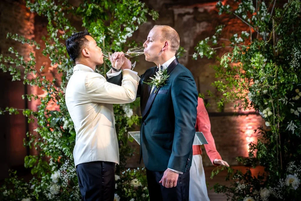 Kevin and James drinking from their glasses of champagne while their arms are interlocked.