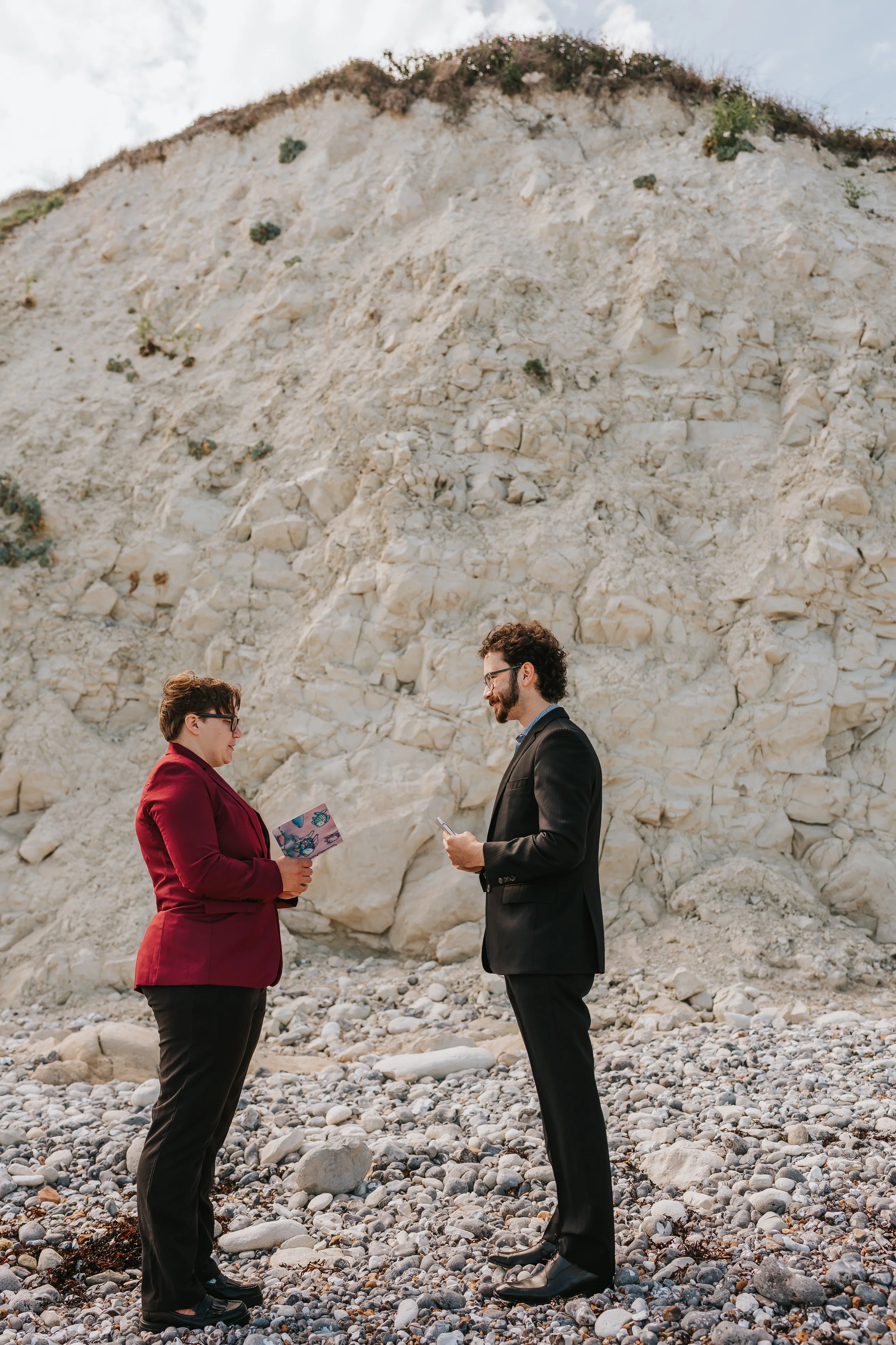 Brigid reading from a notebook while Isaac listens, the white cliff behind them.