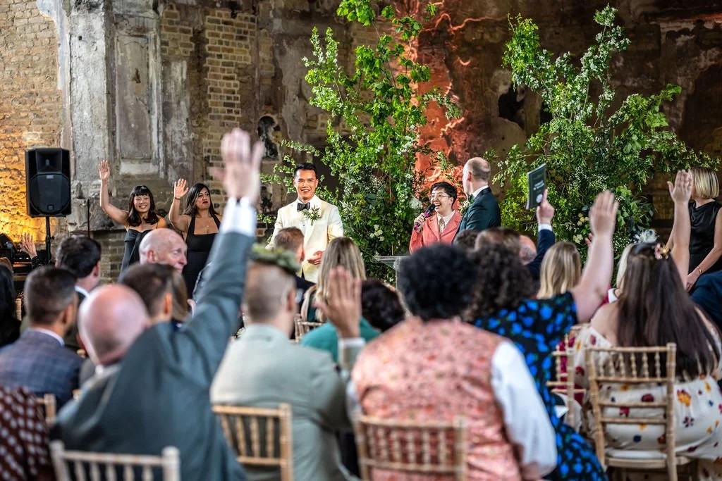 A view from the back of guests raising their hands while Kevin and James look on.