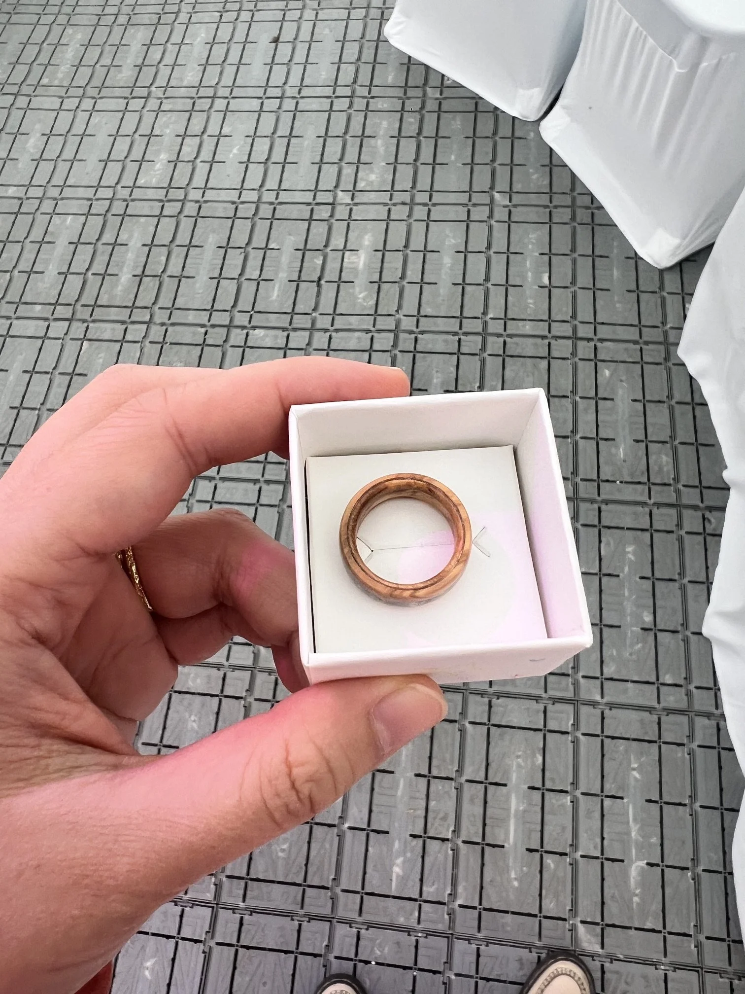 An open white box with a wooden wedding ring inside.