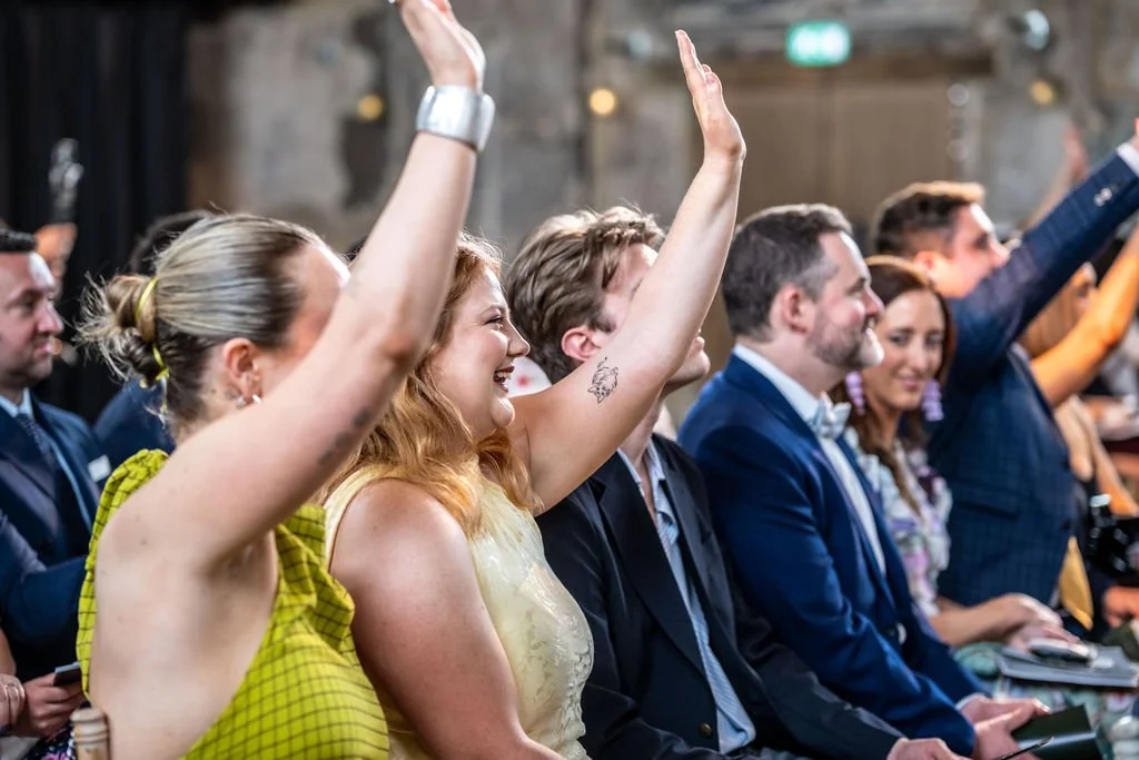 A row of guests, some with their hands raised and smiling.