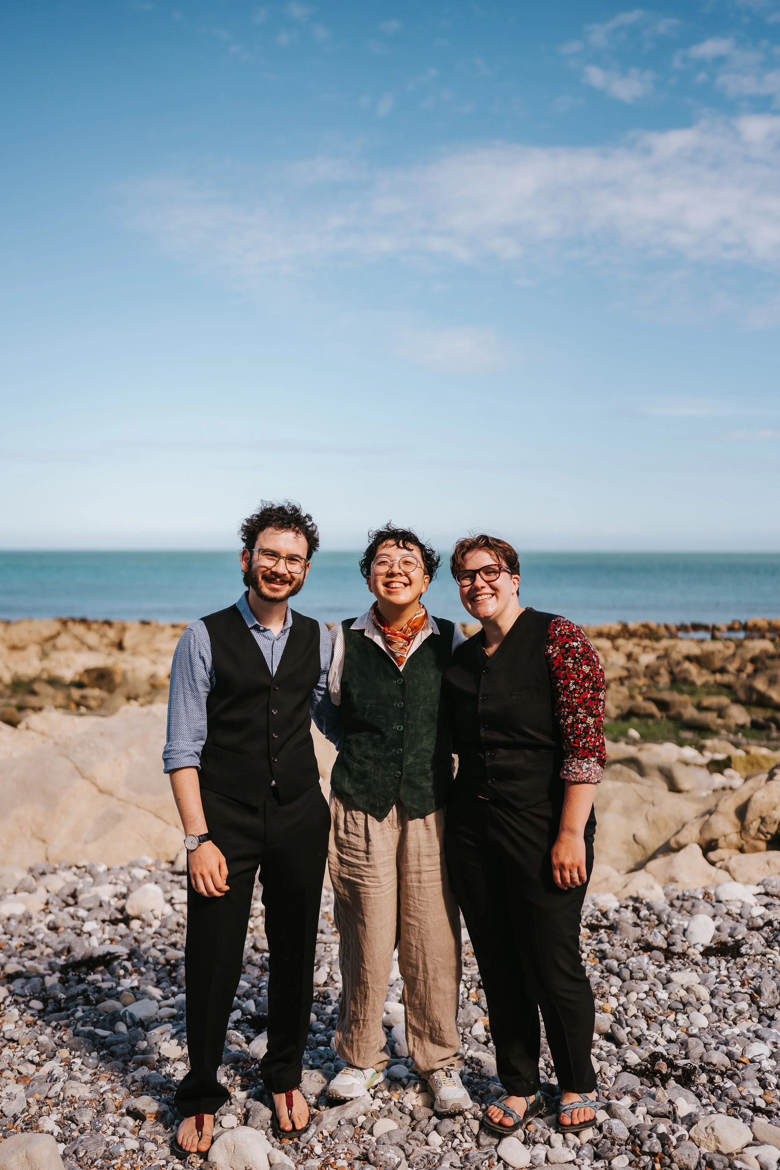 Brigid, Isaac and Holden all smiling and posing for the camera in front of the sea.