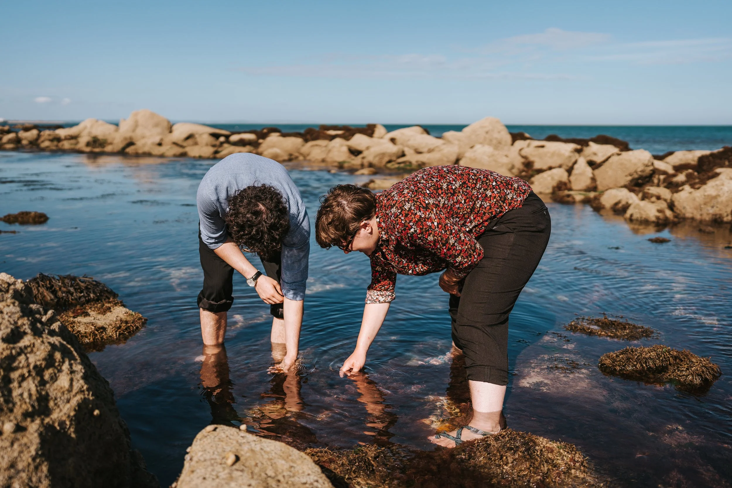Brigid and Isaac bent over, ankle-deep in water as they search for interest objects.