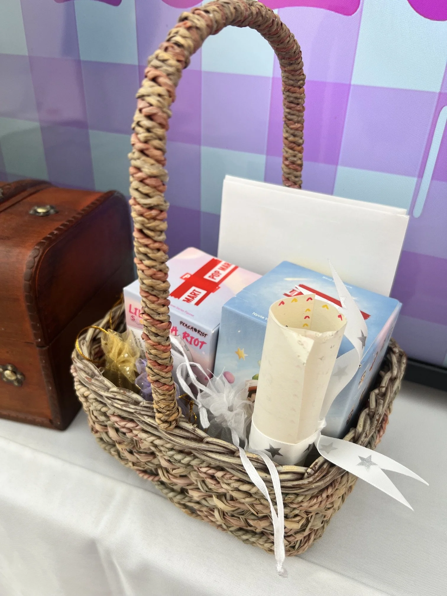 A basket containing a number of items, including blind boxes, a scroll, envelopes, and organza pouches.