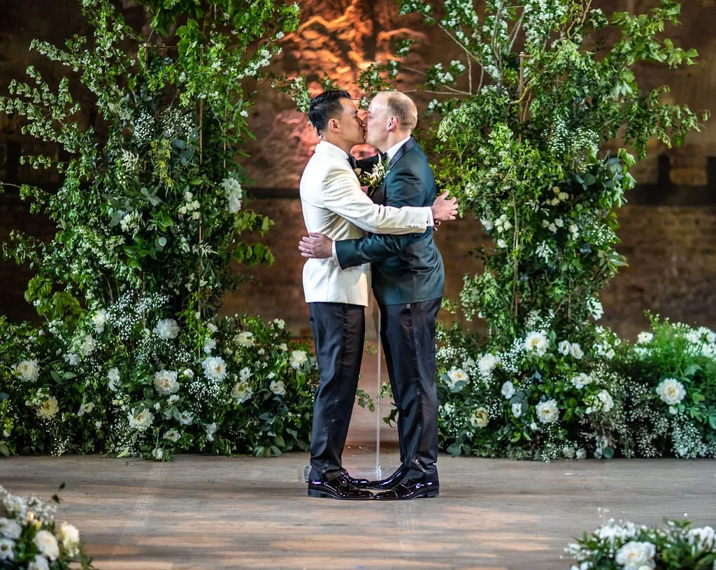 Kevin and James kissing, perfectly framed by the broken floral arch.