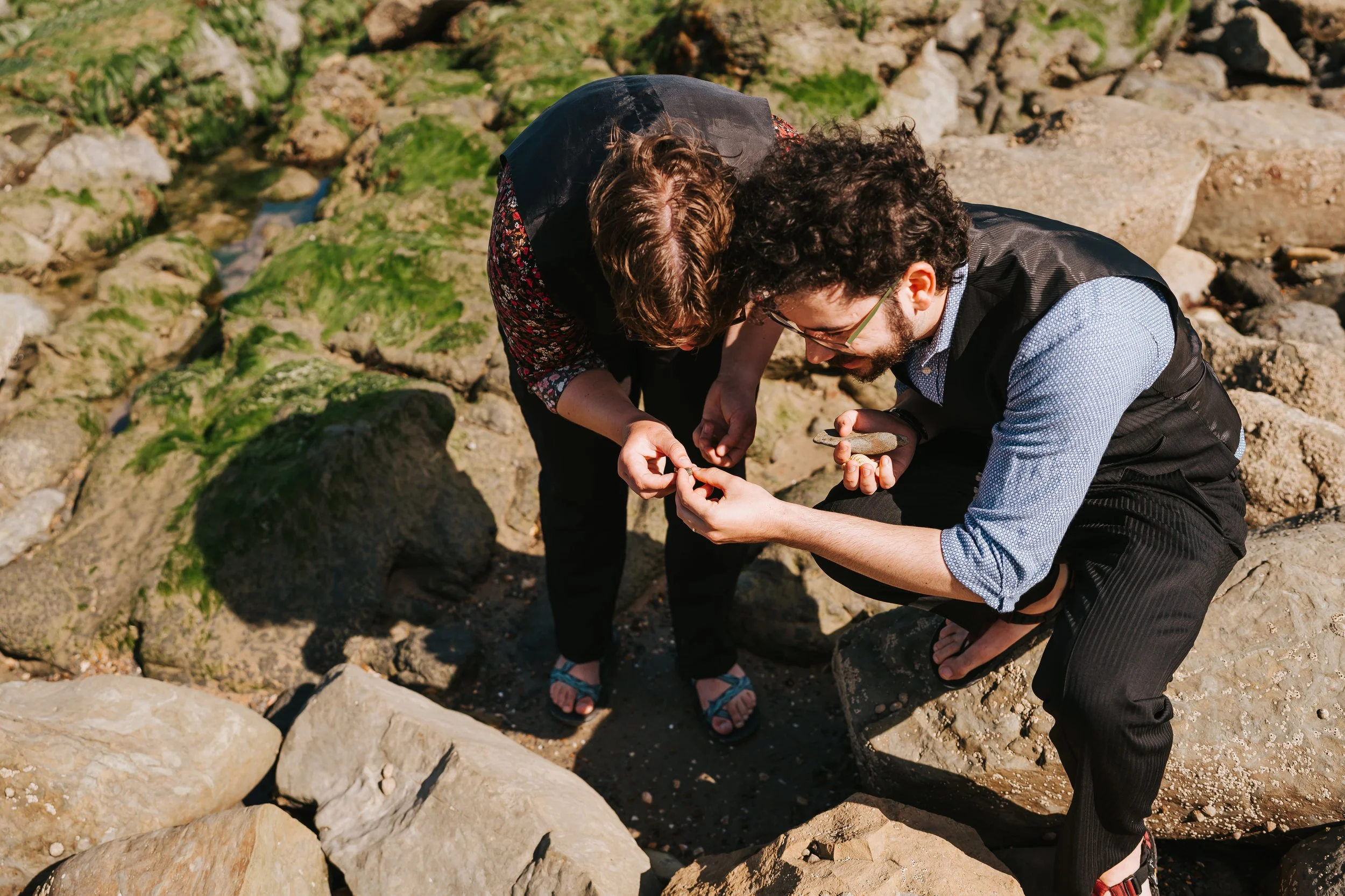 Brigid and Isaac bent over examining something small that they're holding, in the midst of big rocks.