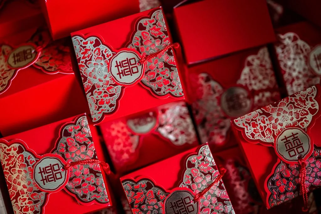 A pile of red wedding favour boxes with the Chinese character for double happiness on them, a traditional symbol for marriage.