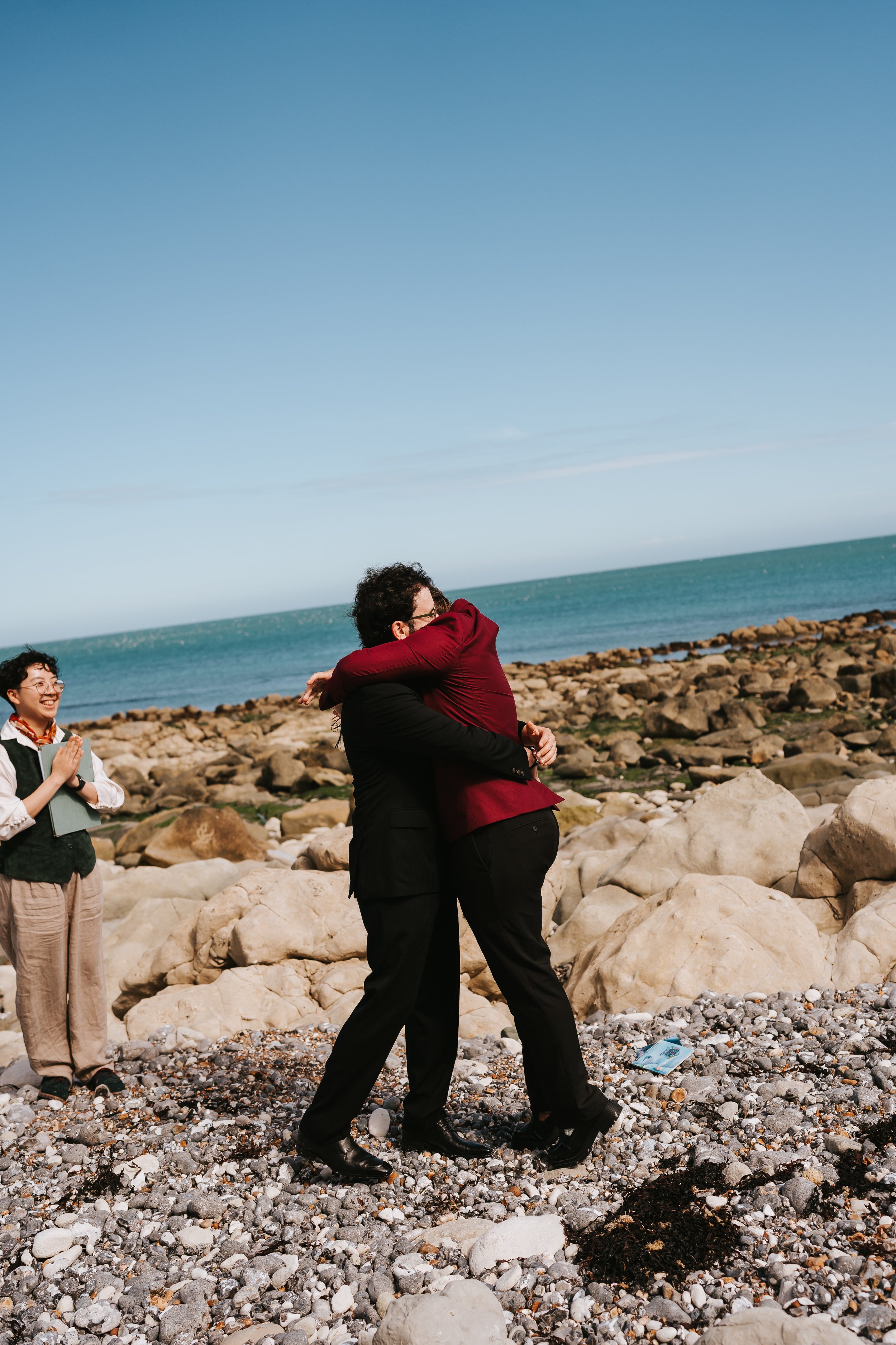 Brigid and Isaac hugging each other tightly while Holden their celebrant is clapping.