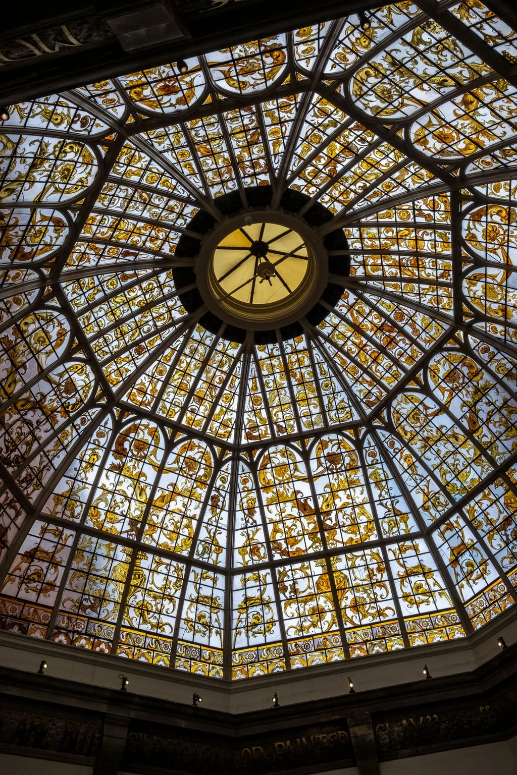 A domed stained-glass ceiling in the Battersea Arts Centre. The design looks intricate and the glass is stained a golden colour.