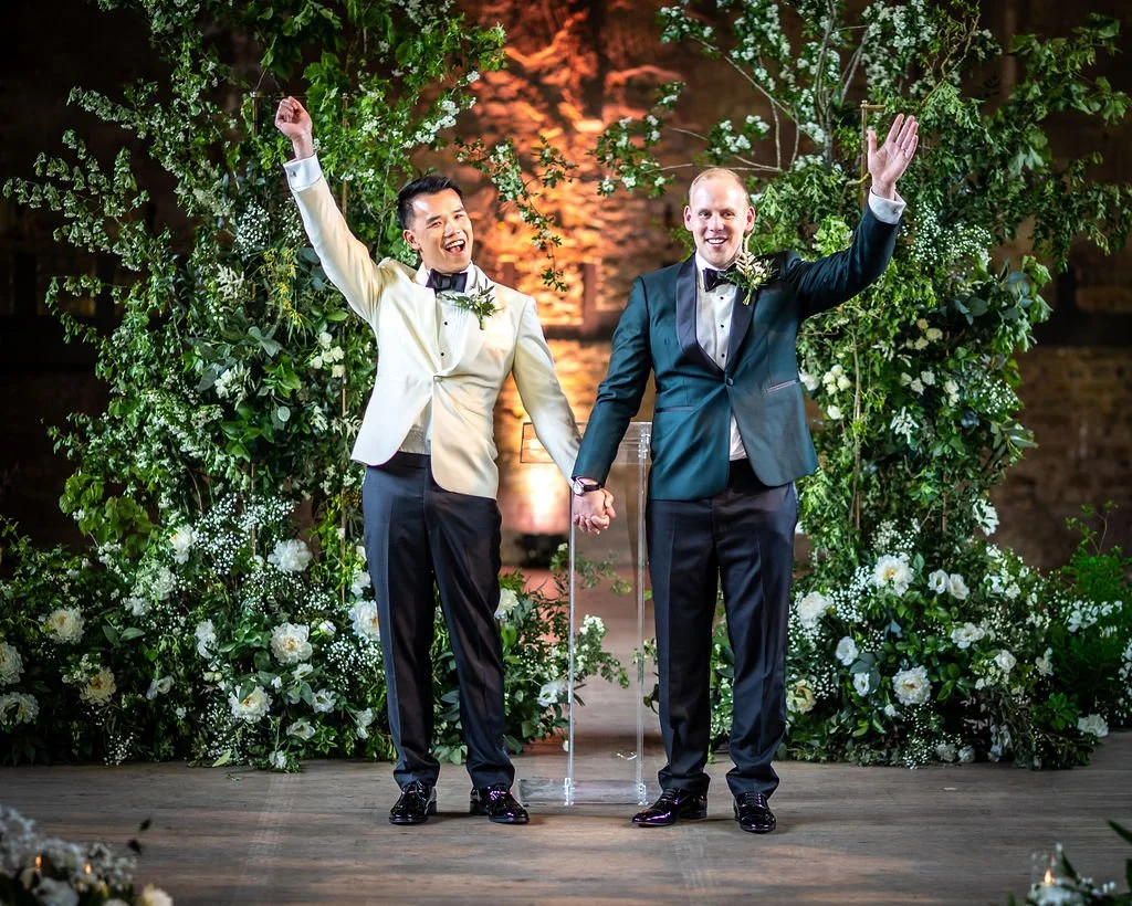 Kevin and James holding hands, and each has their other arm raised in the air in celebration.