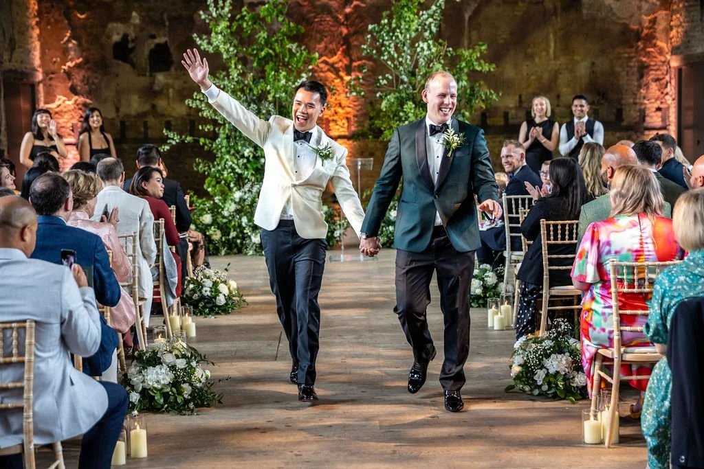 Kevin and James dancing back down the aisle, their joyful energy apparent, while guests clap.