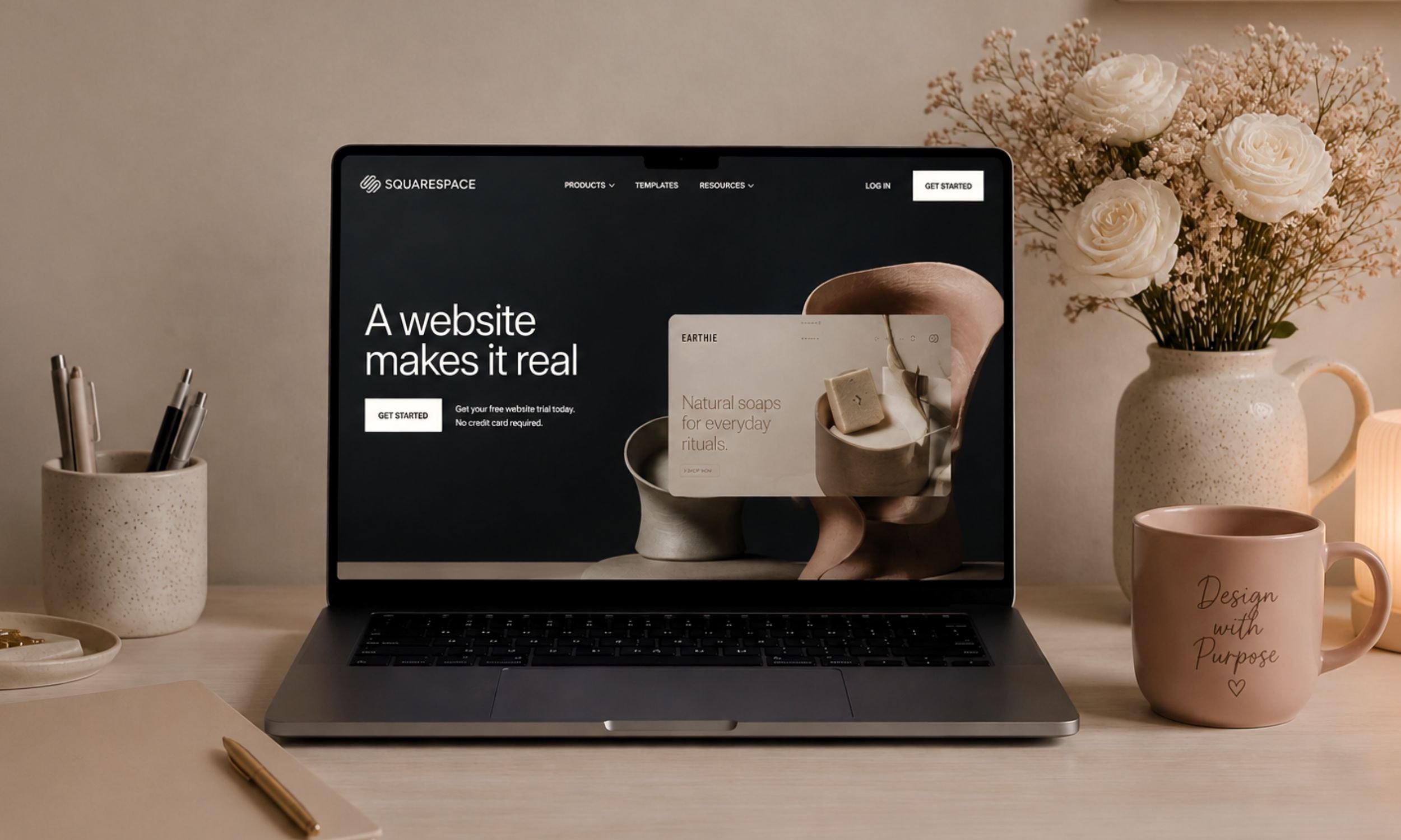 A laptop displaying the Squarespace website on a wooden desk, surrounded by a beige pen holder filled with pens, a pink mug with text, a notebook with a pen on top, a vase of white roses and baby's breath flowers, and a beige jar with a handle.