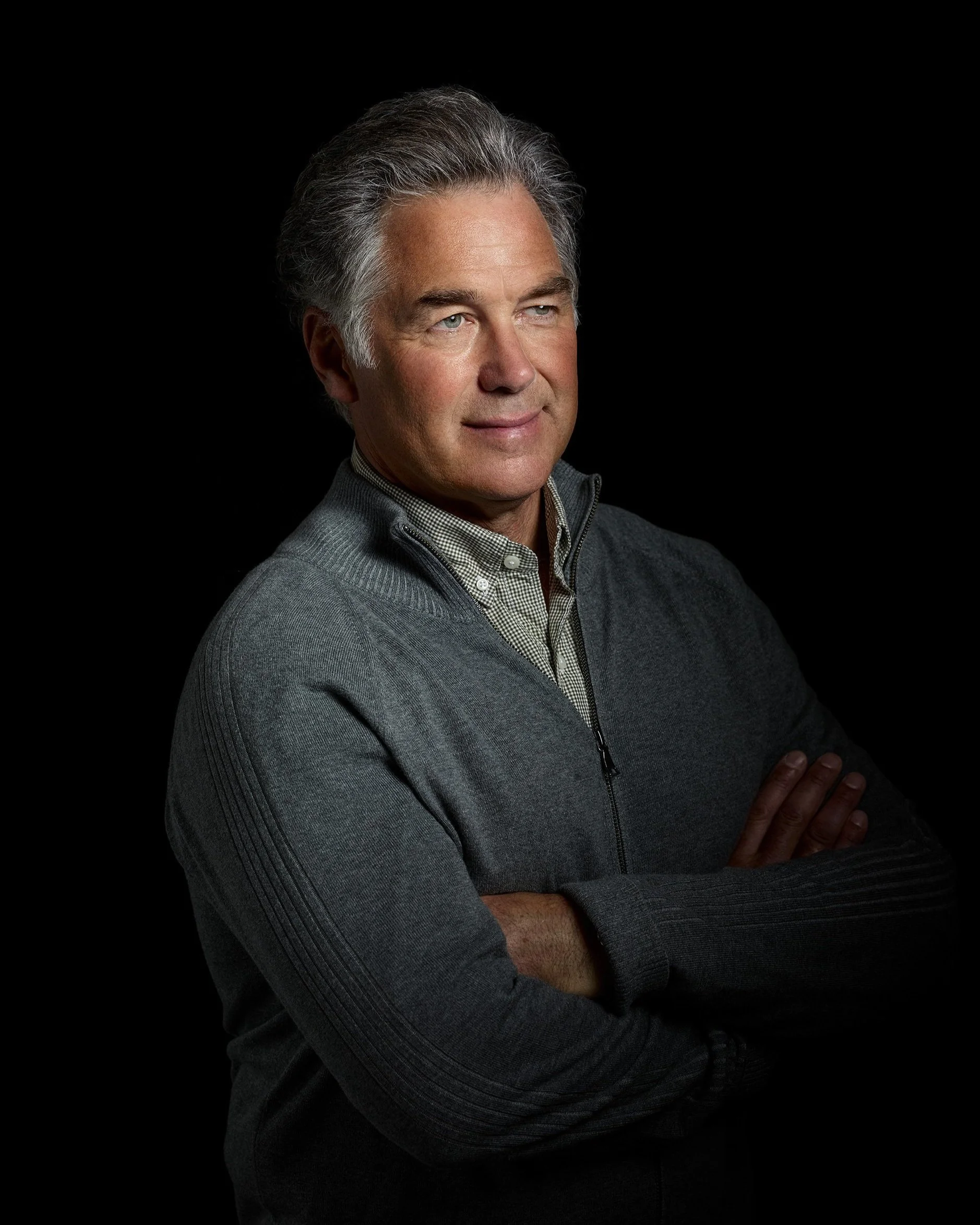 Professional Headshots, man; dramatic light in studio; black backdrop; relaxed gaze staring off camera; classic, business-ready presentation.
