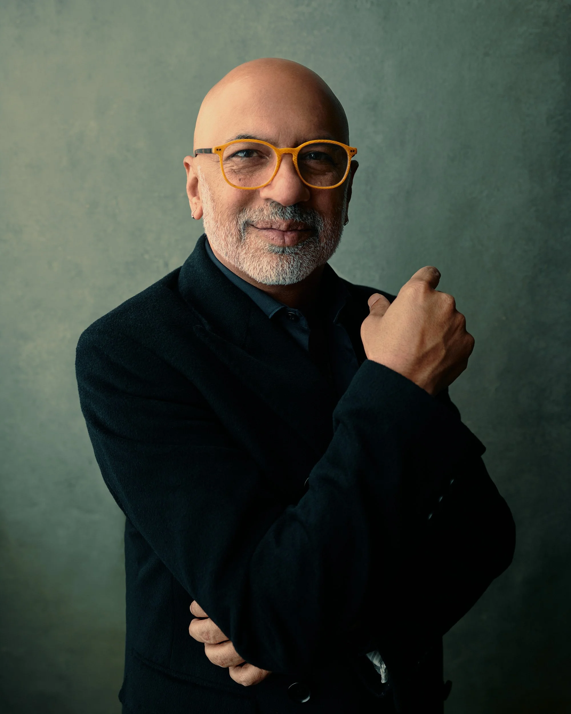 Team headshot of man in black shirt and glasses with arms crossed against gray studio background