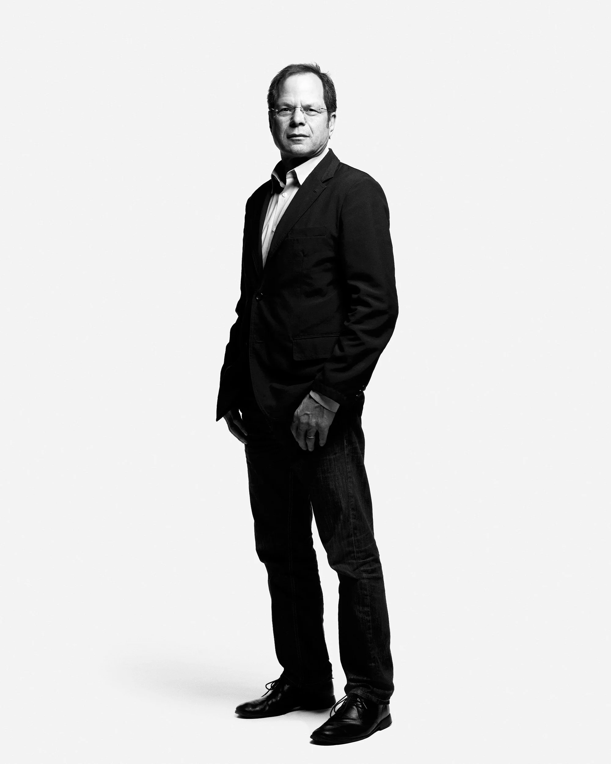 Full-length team headshot of man in dark suit with white studio backdrop