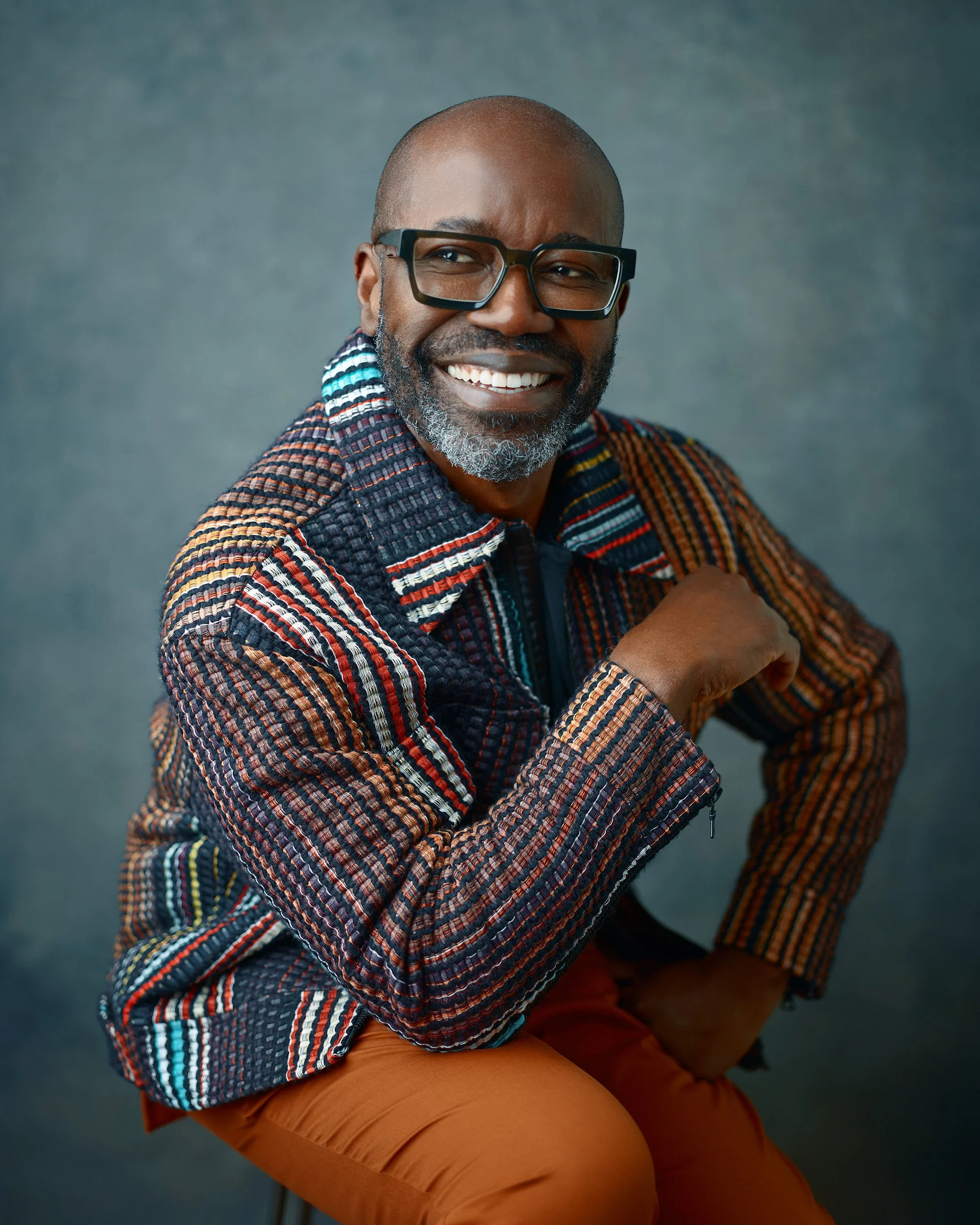 Professional Headshots, man; even studio strobe; light blue textured backdrop; seated confident posture; modern, minimal style with calm expression.
