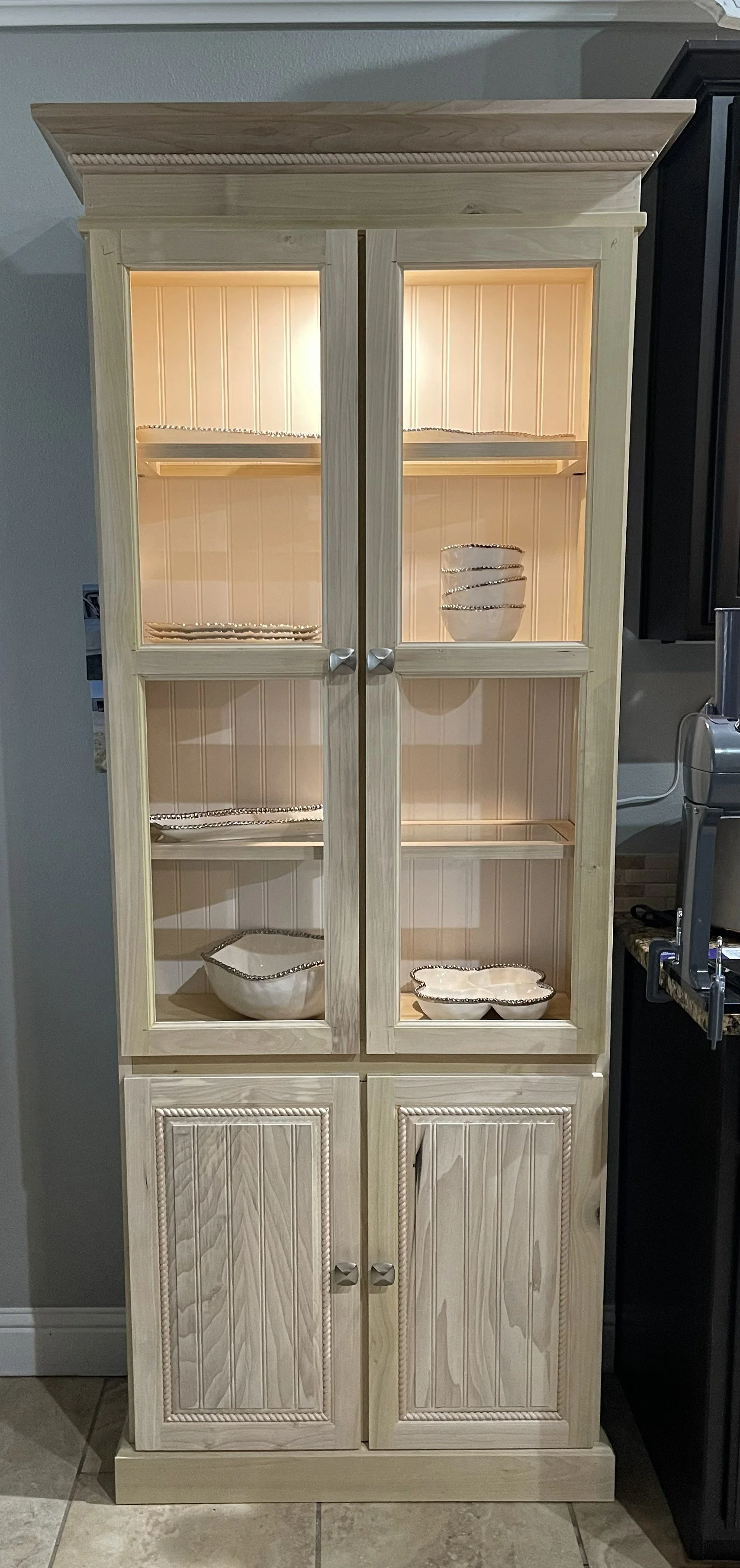 A wooden display cabinet with glass doors containing decorative ceramic bowls and plates.