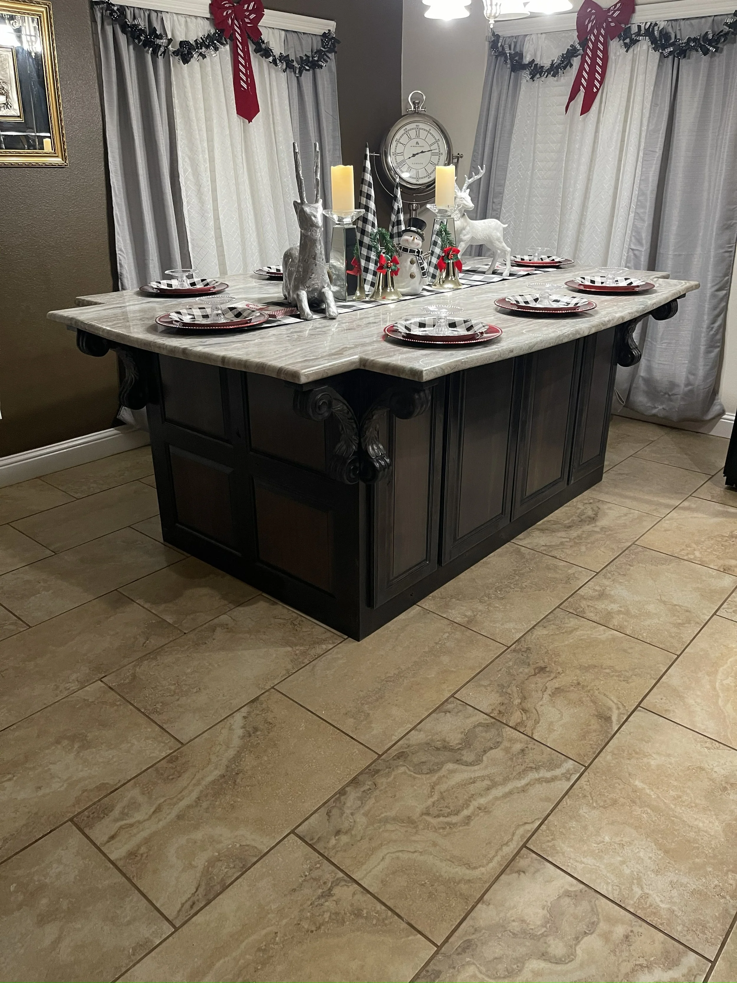 A dining table decorated for Christmas with black and white checkered placemats, red and black plates, and glassware. The table has a holiday centerpiece with silver reindeer figurines, a snowman, red bows, candles, and black and white checkered ribb
