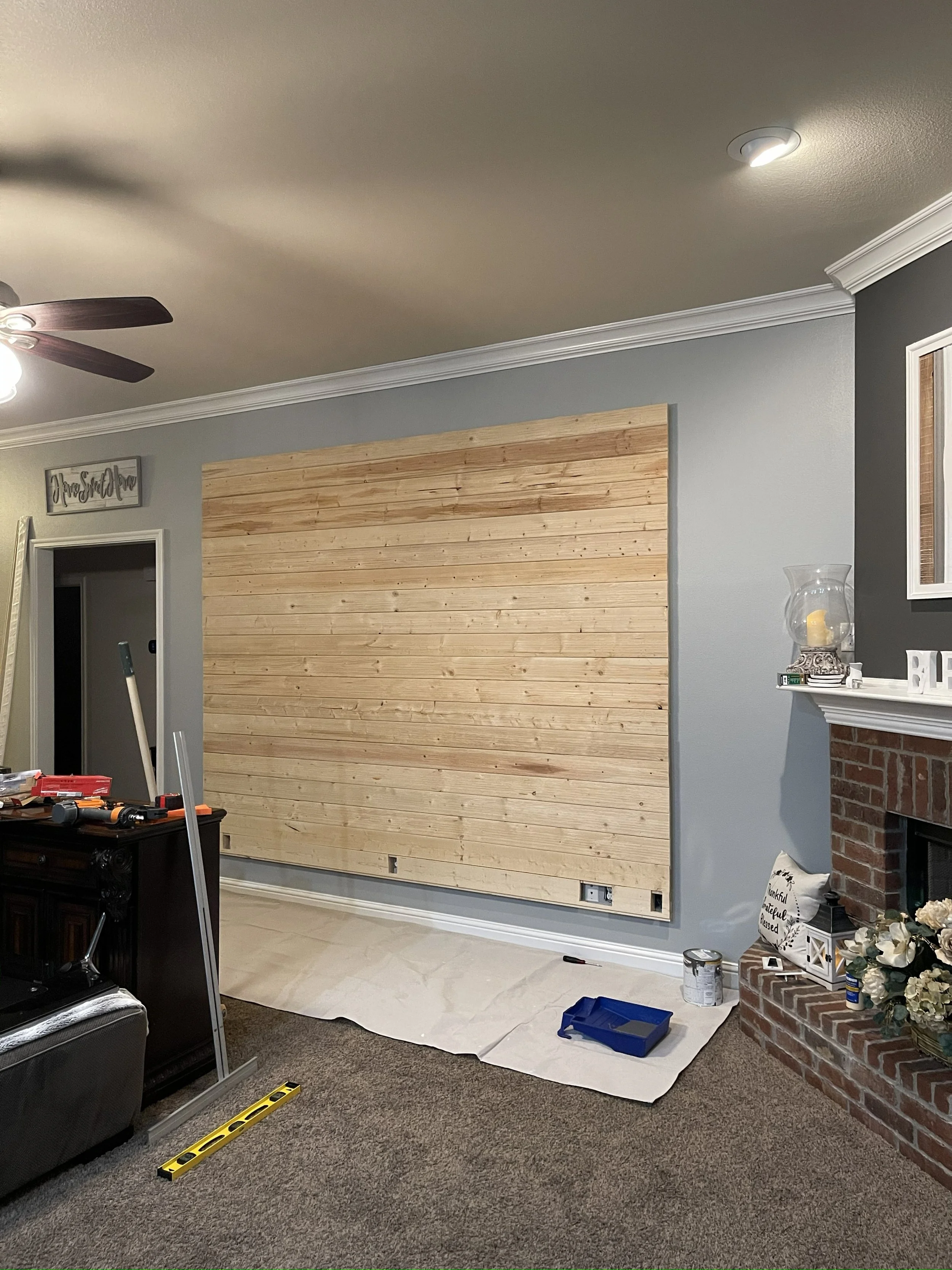 Living room with a newly installed wooden wall panel, tools, and supplies for construction or renovation project.