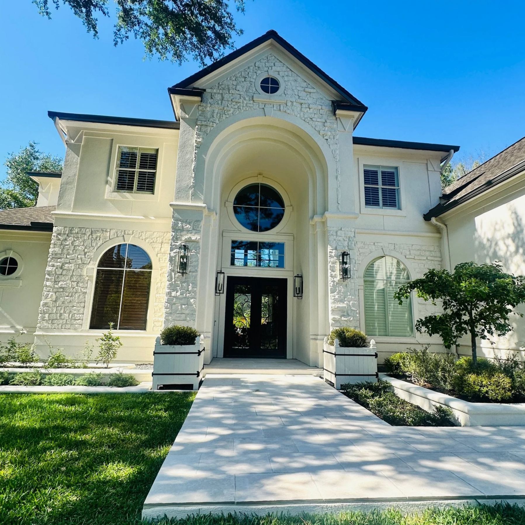Front entry of the Willowcrest Place home in Cochran's Crossing: white stone arch, tumbled-edge porcelain walk, white Versailles planters and stucco raised beds by Petal Organic, The Woodlands TX
