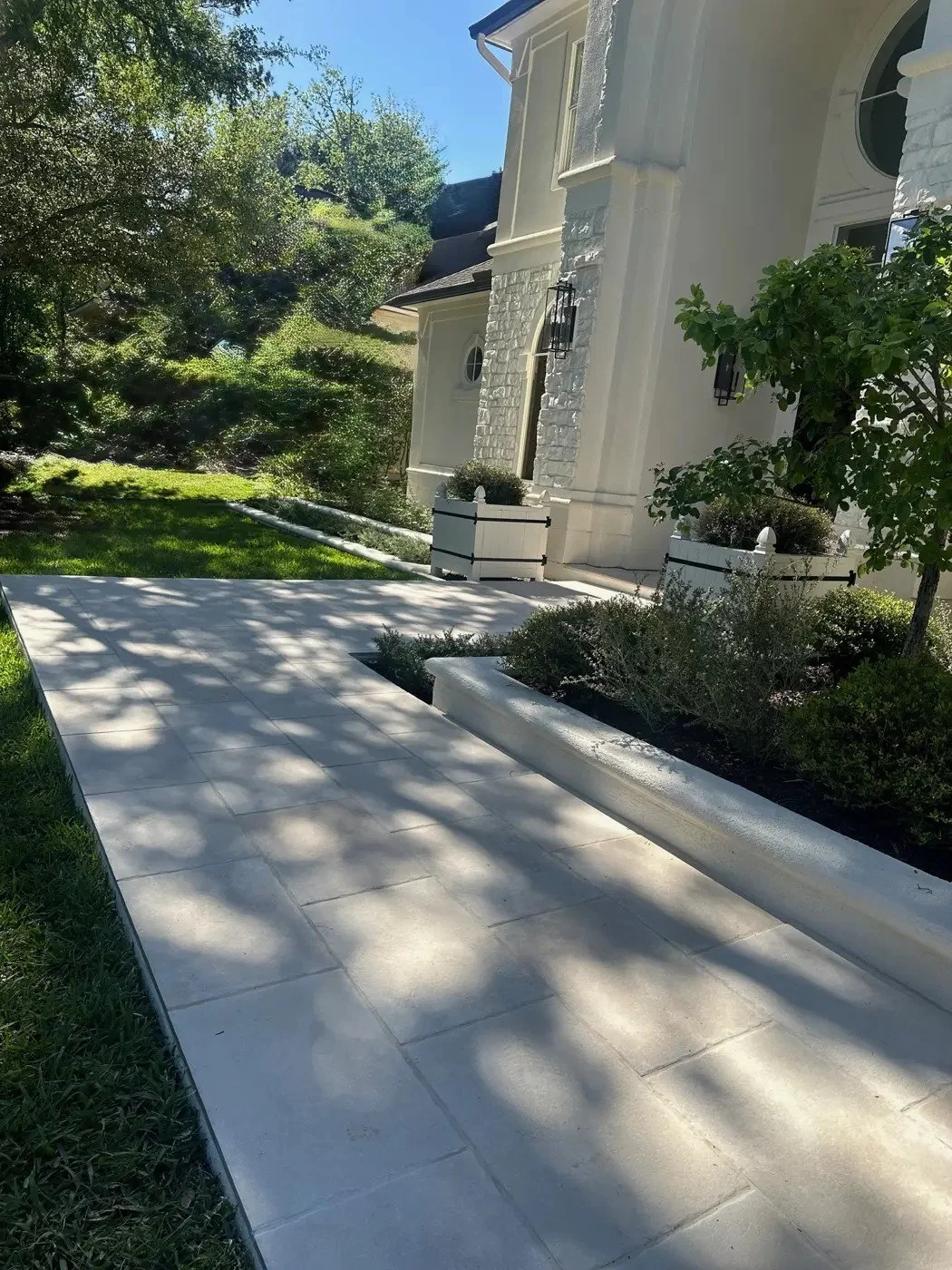 Finished La Pietra tumbled-edge porcelain entry walk running between the lawn and a stucco raised bed toward white Versailles planters, The Woodlands TX