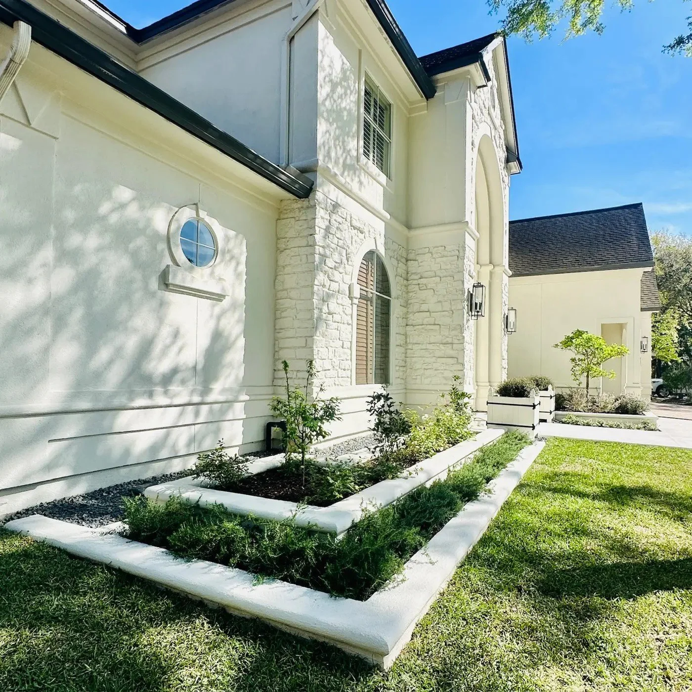 Two tiers of white stucco raised beds and concrete curbing with prostrate rosemary along the side of a white stone house, Cochran's Crossing, The Woodlands TX