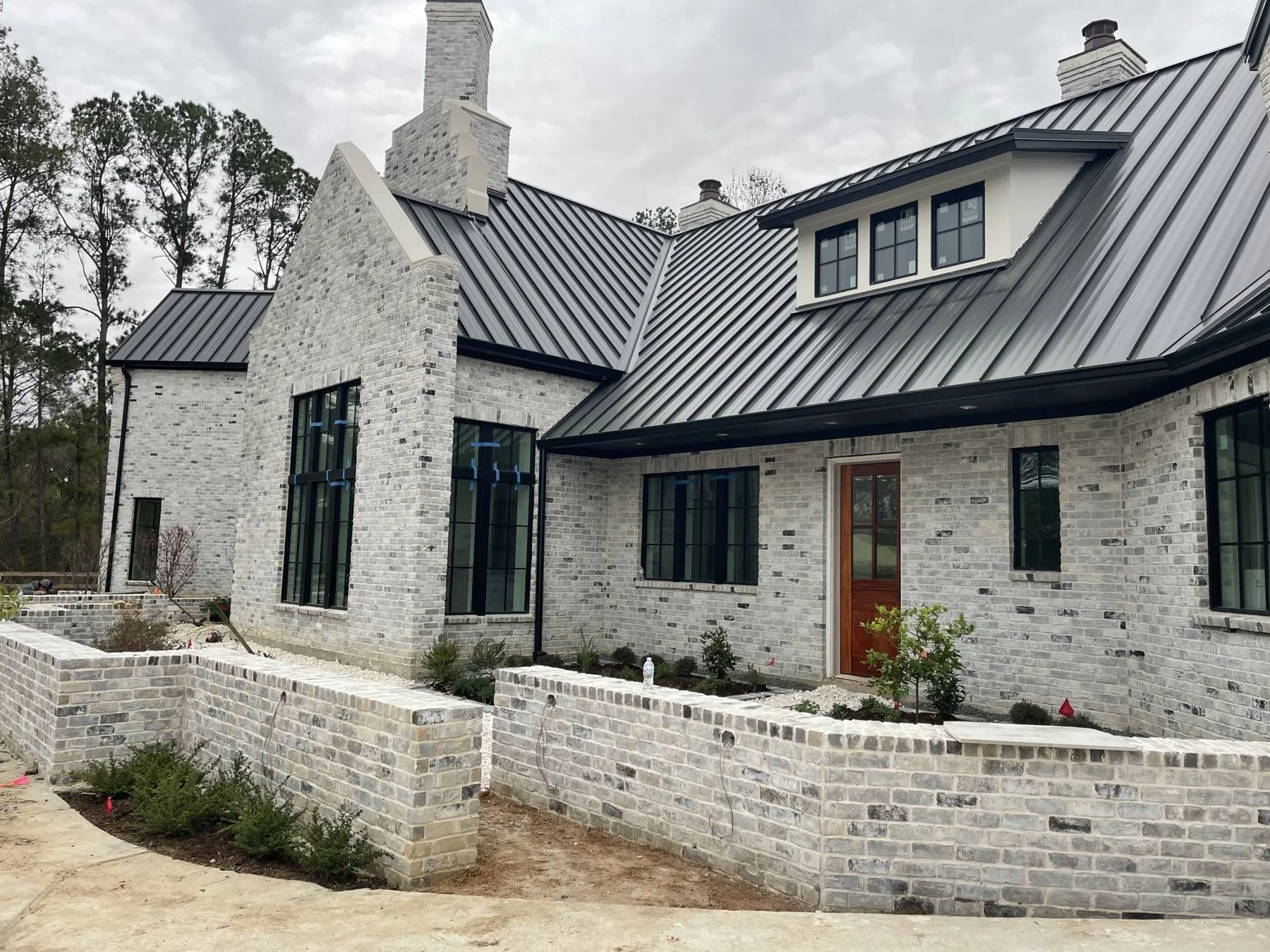 White-brick farmhouse with a standing-seam metal roof and raised courtyard beds in matching white brick, Wilderness Trail, Friendswood TX