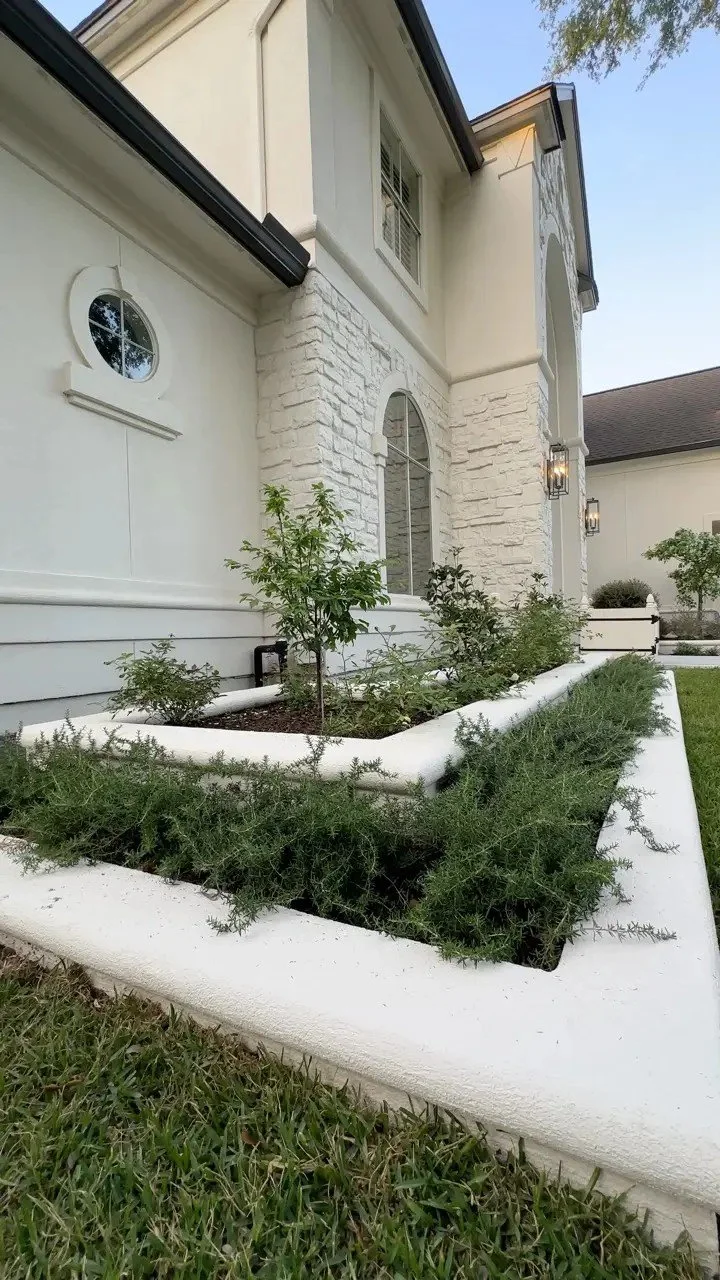 Stucco raised beds and rosemary trough at dusk with the entry lanterns lit, a Petal Organic landscape in Cochran's Crossing, The Woodlands TX